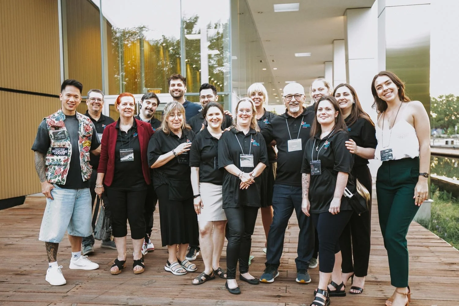 Group of people smiling and posing for a photo outdoors near a modern building with large glass windows.