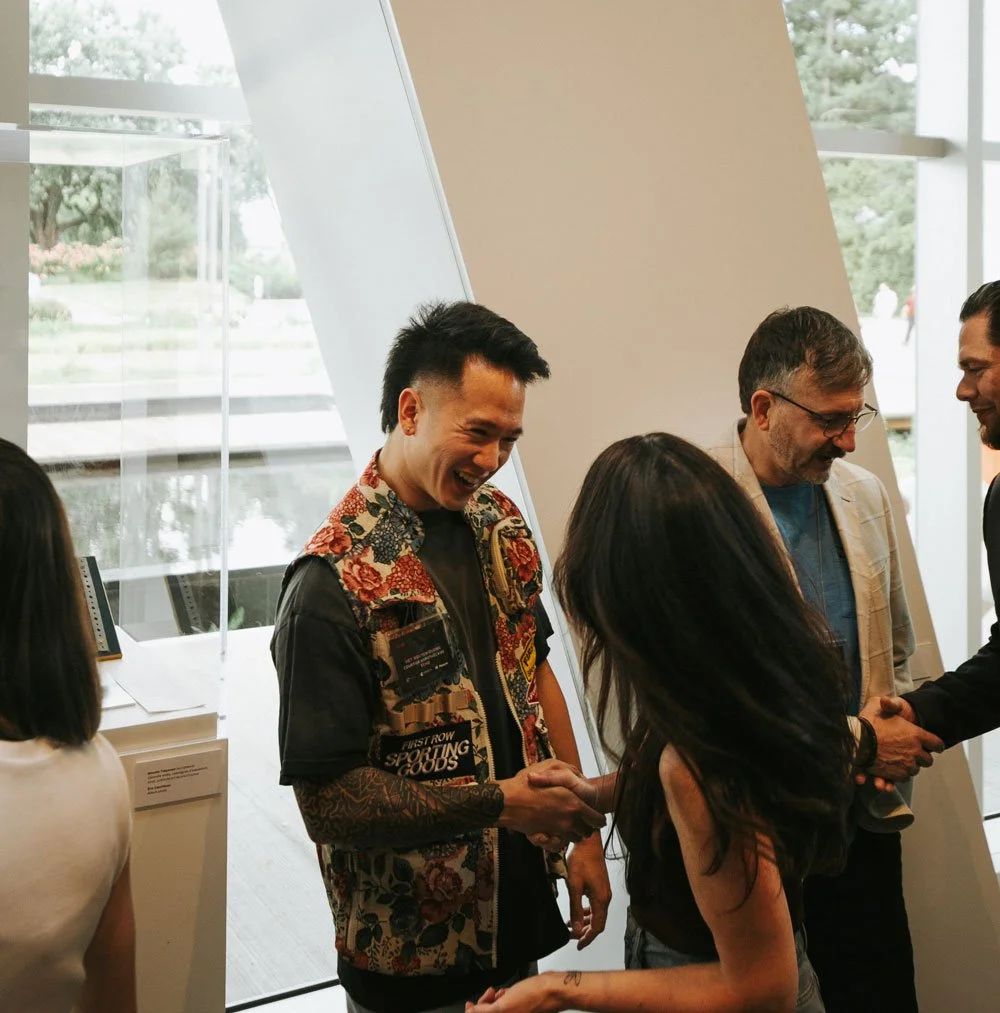Man shaking hands with a woman in an indoor space with large windows, while other people look on