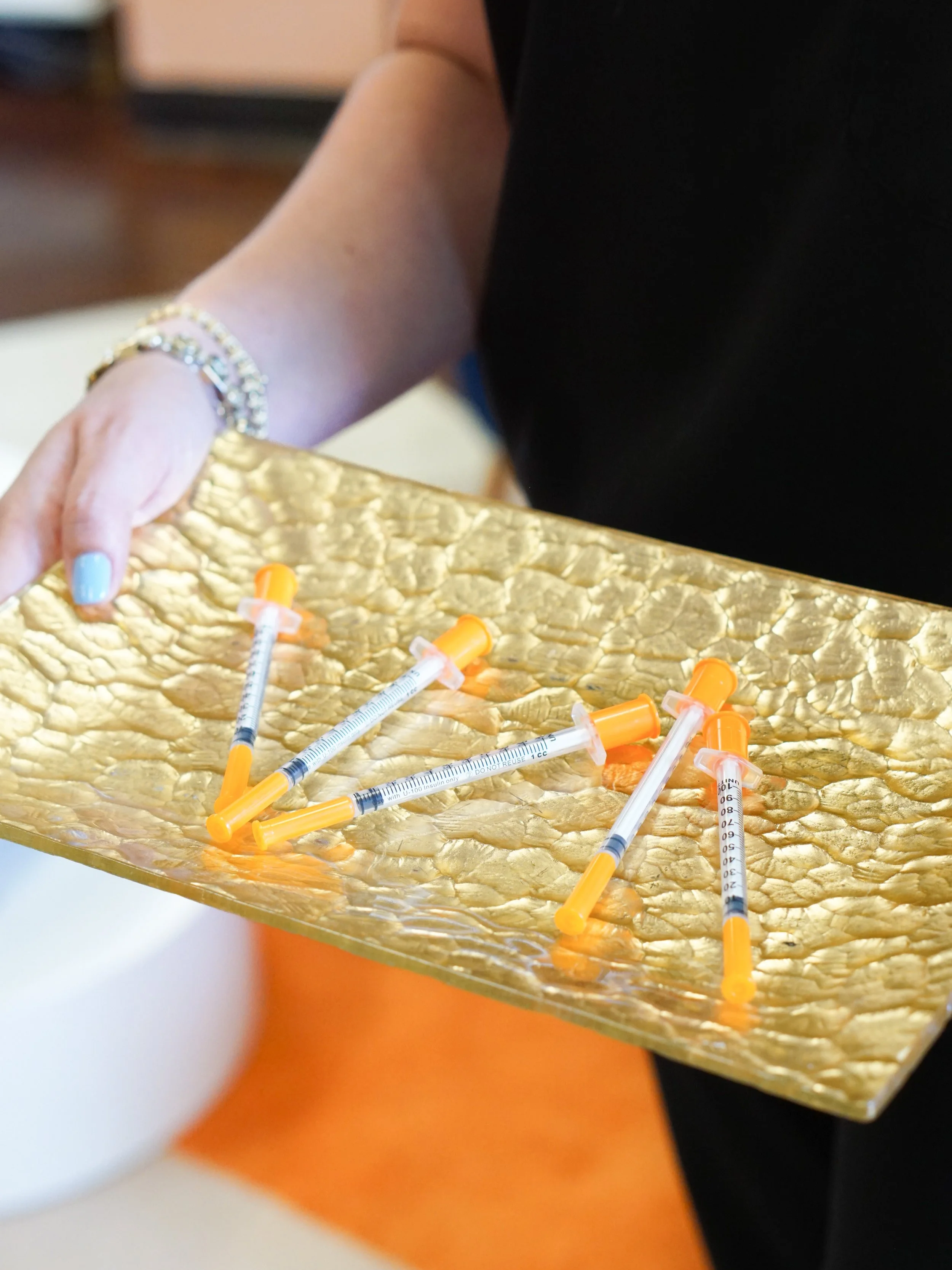 Person holding a golden tray with several unused syringes with orange caps.