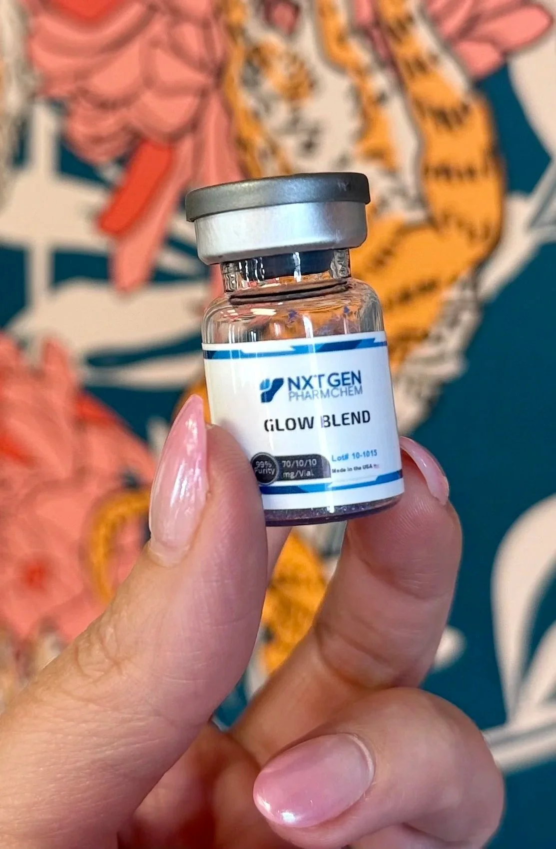 A small glass vial labeled 'Glow Blend' held between a person's thumb and index finger, with a colorful abstract background.