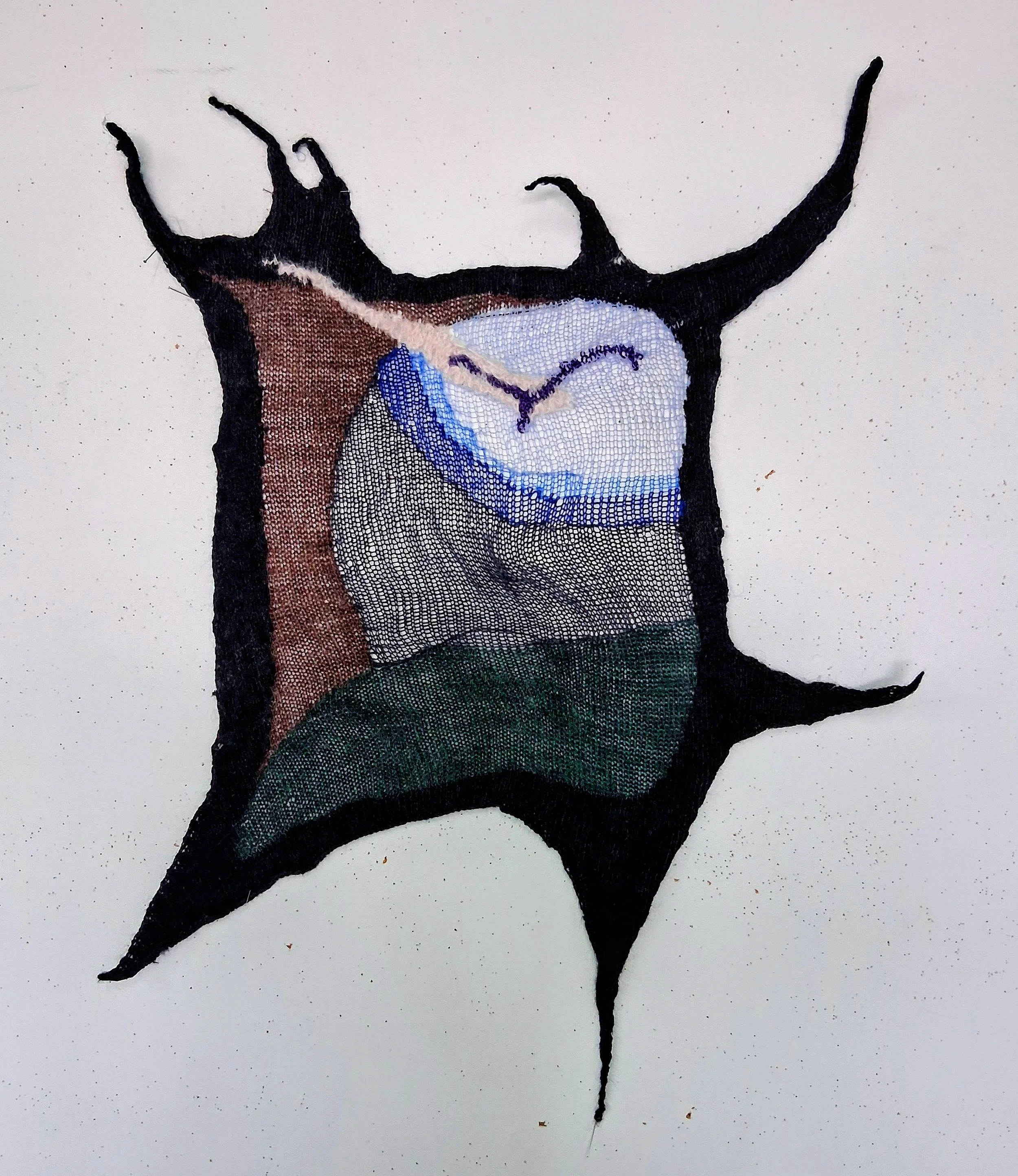 Cadre Corbeau réalisé en intarsia avec le tricot machine. Le cadre gothique est noir, à l'intérieur est un paysage stylisé avec l'herbe verte, un arbre brun, et un oiseau mauve au milieu du ciel en dégradé de bleus.