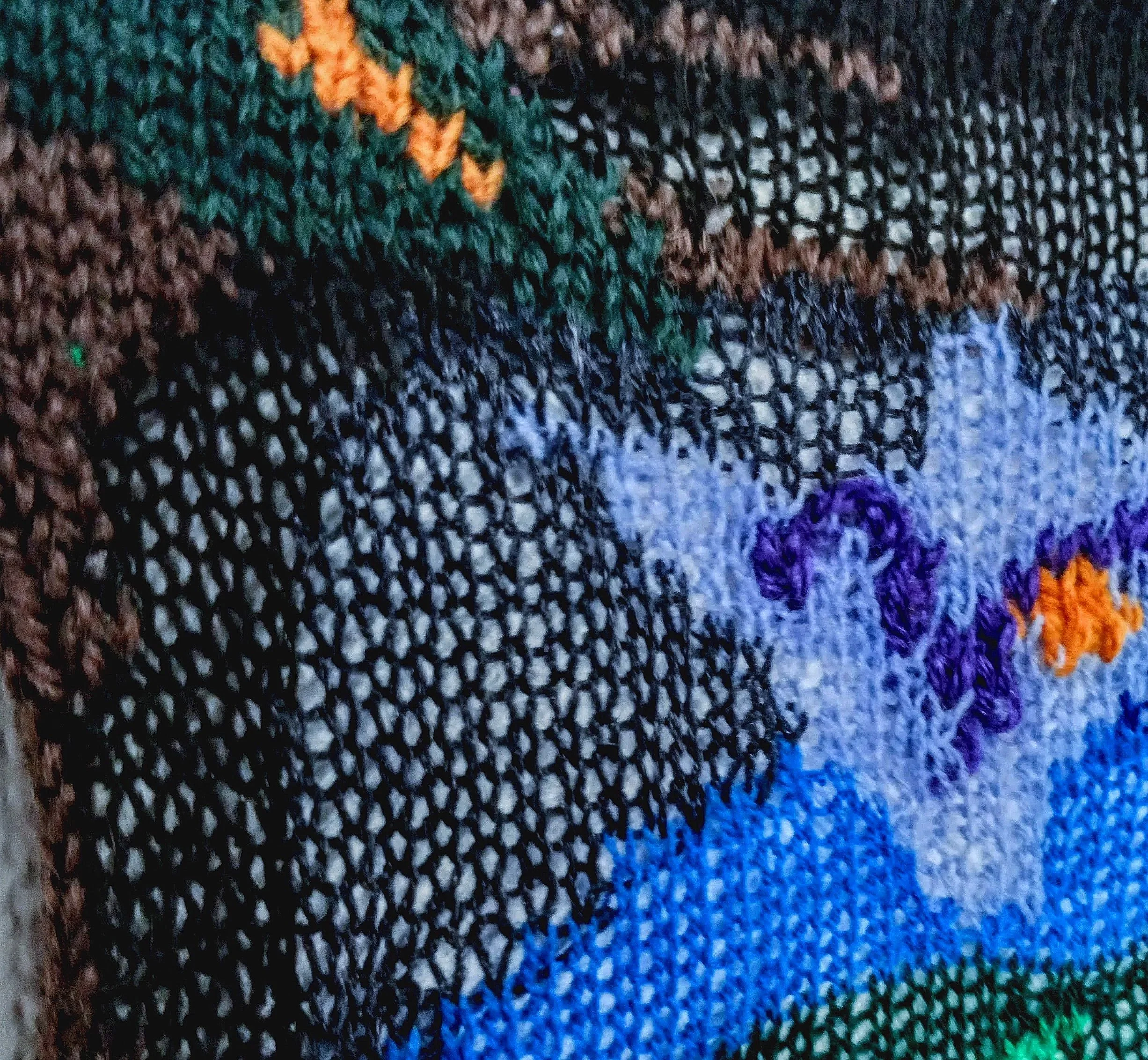 Détail de la pièce tricotée en intarsia Tranquillement, Différement, de la série de tricot-peinture. On y voit un arbre brun et vert, un ciel dans des dégradés de bleu, un oiseau mauve et un soleil et un éclat orange.