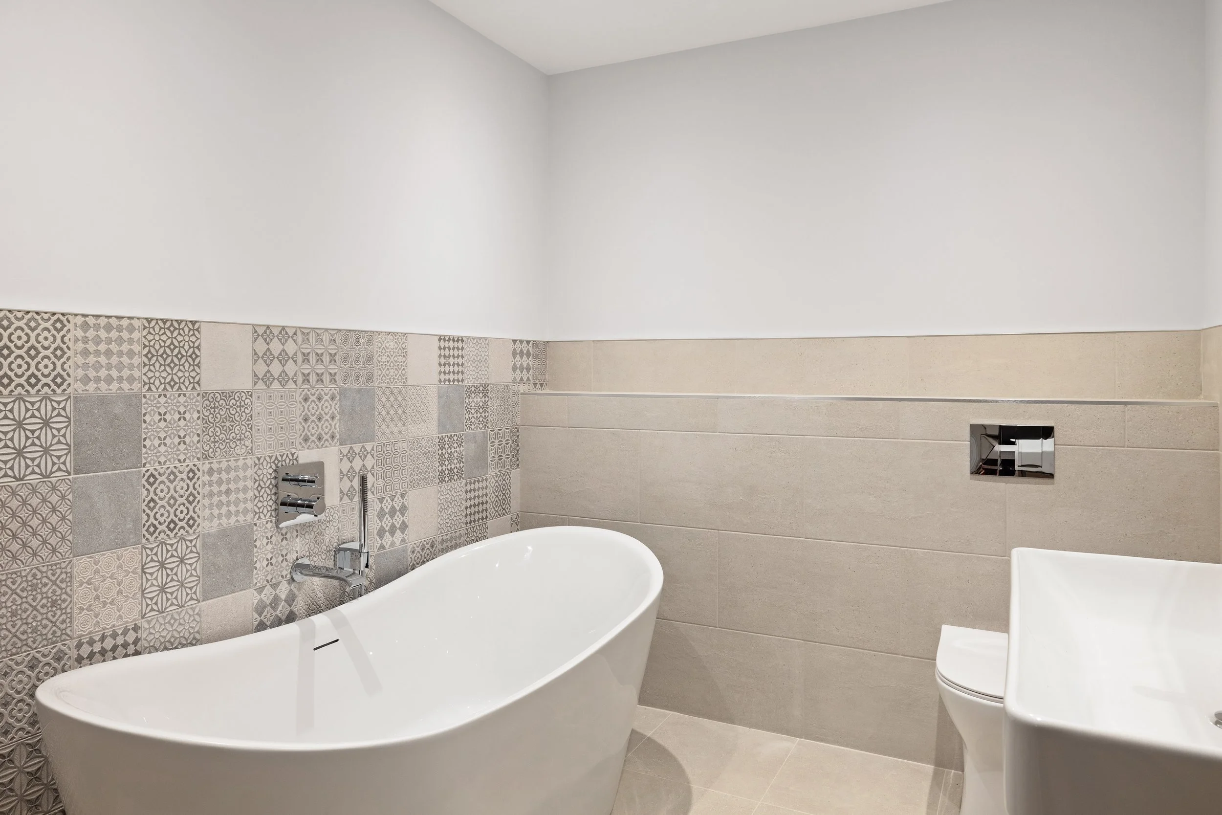 Modern bathroom with a freestanding bathtub, decorative tiled wall, toilet, and white walls.