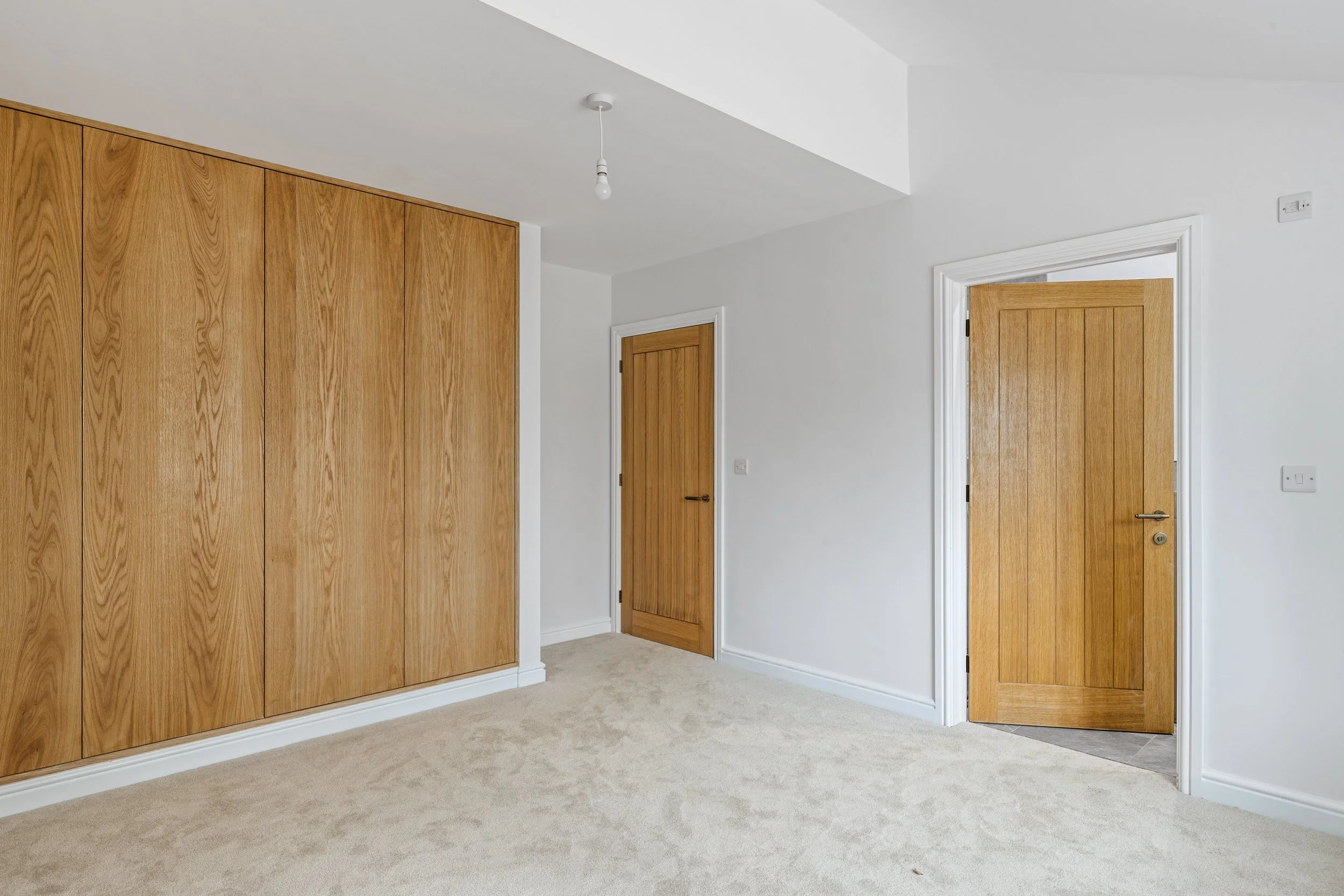 Empty room with beige carpet, white walls, wooden doors, and large built-in wooden wardrobe.