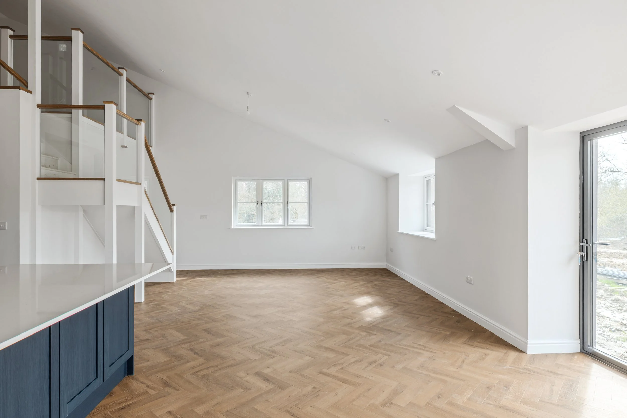 Empty living room with white walls, hardwood floor, three windows, and a glass door leading outside.
