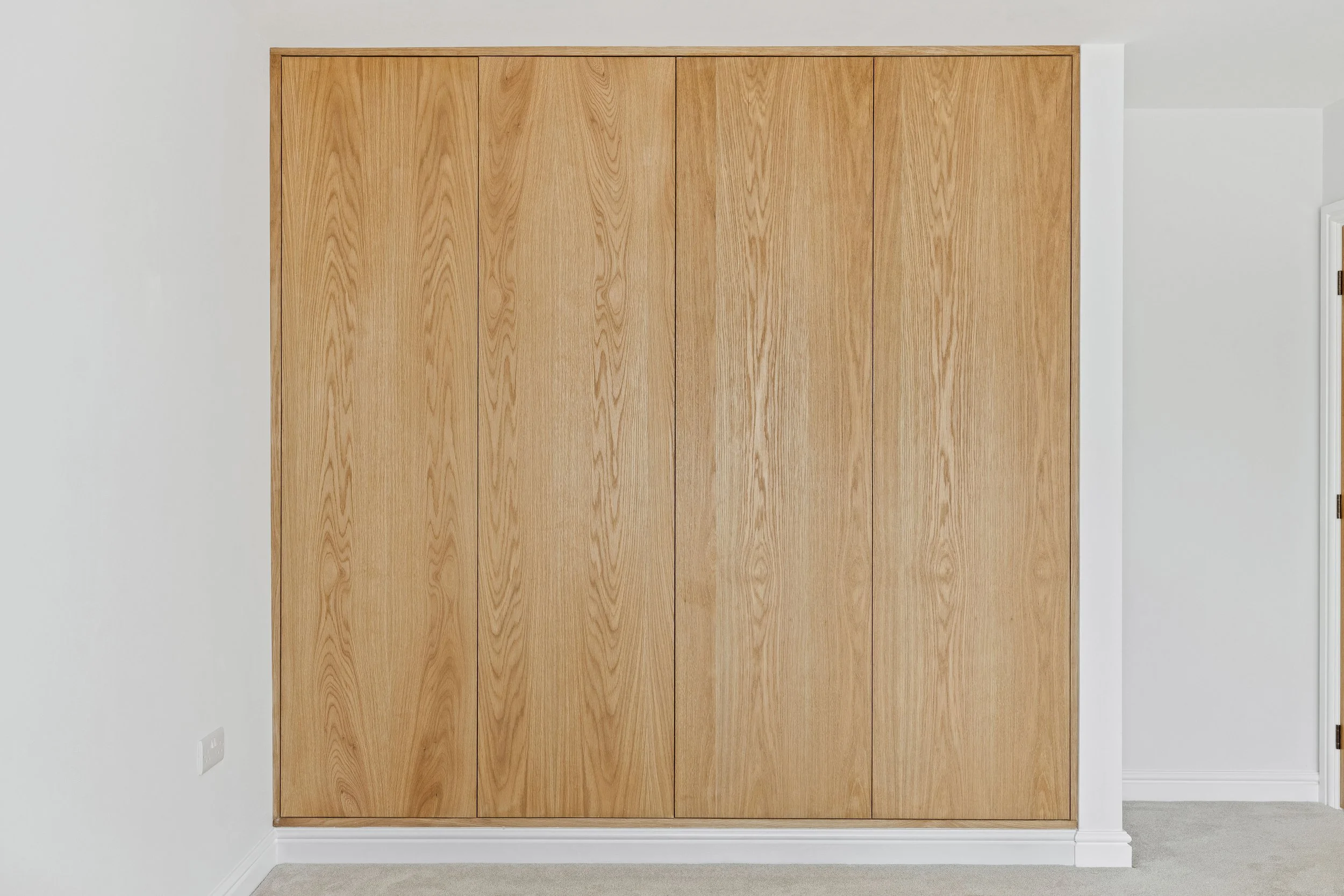 Wooden closet doors in a room with white walls and carpeted flooring.