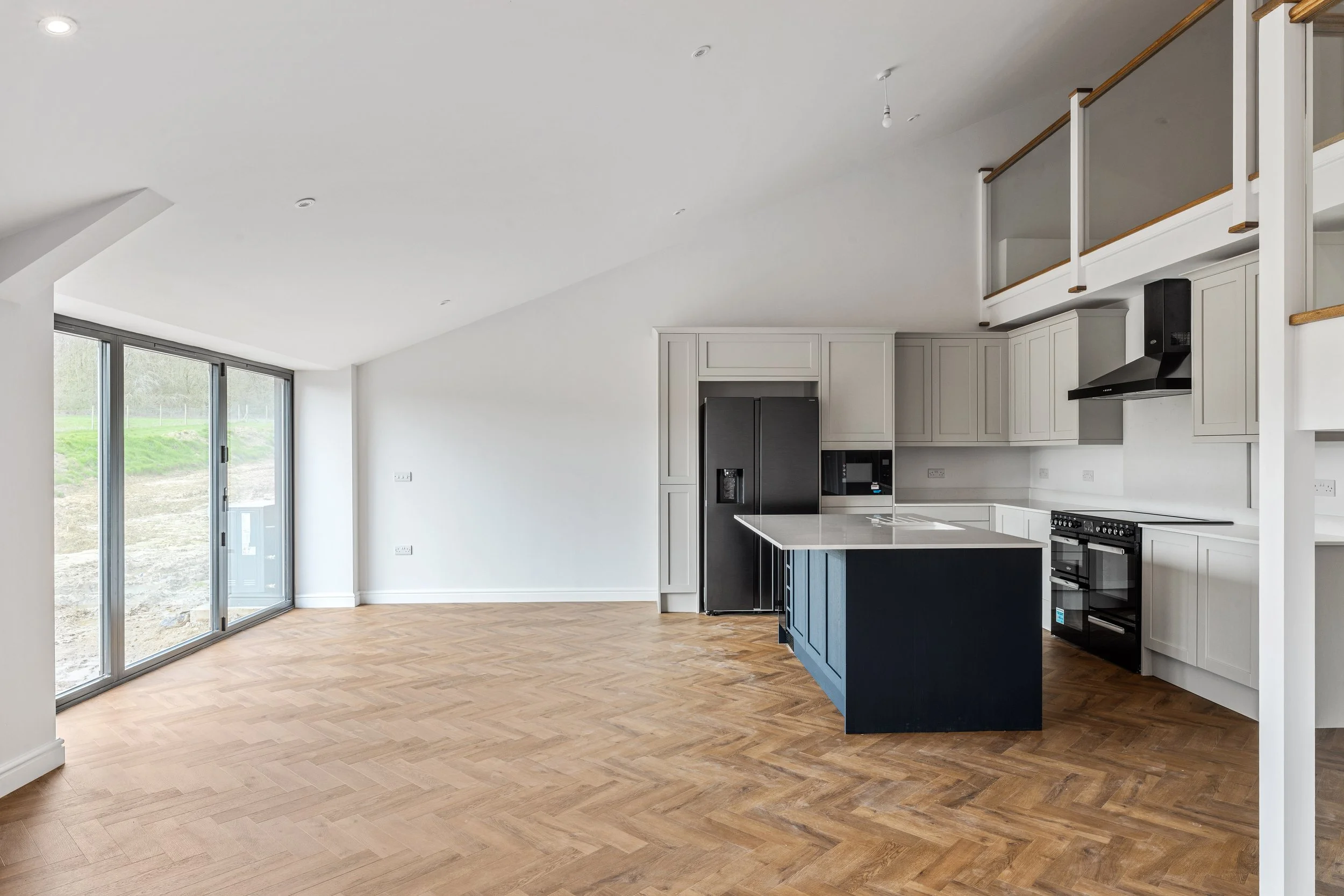 Open plan kitchen and living area with white cabinetry, black appliances, and a kitchen island with blue base, hardwood floors, and sliding glass doors to the outside.