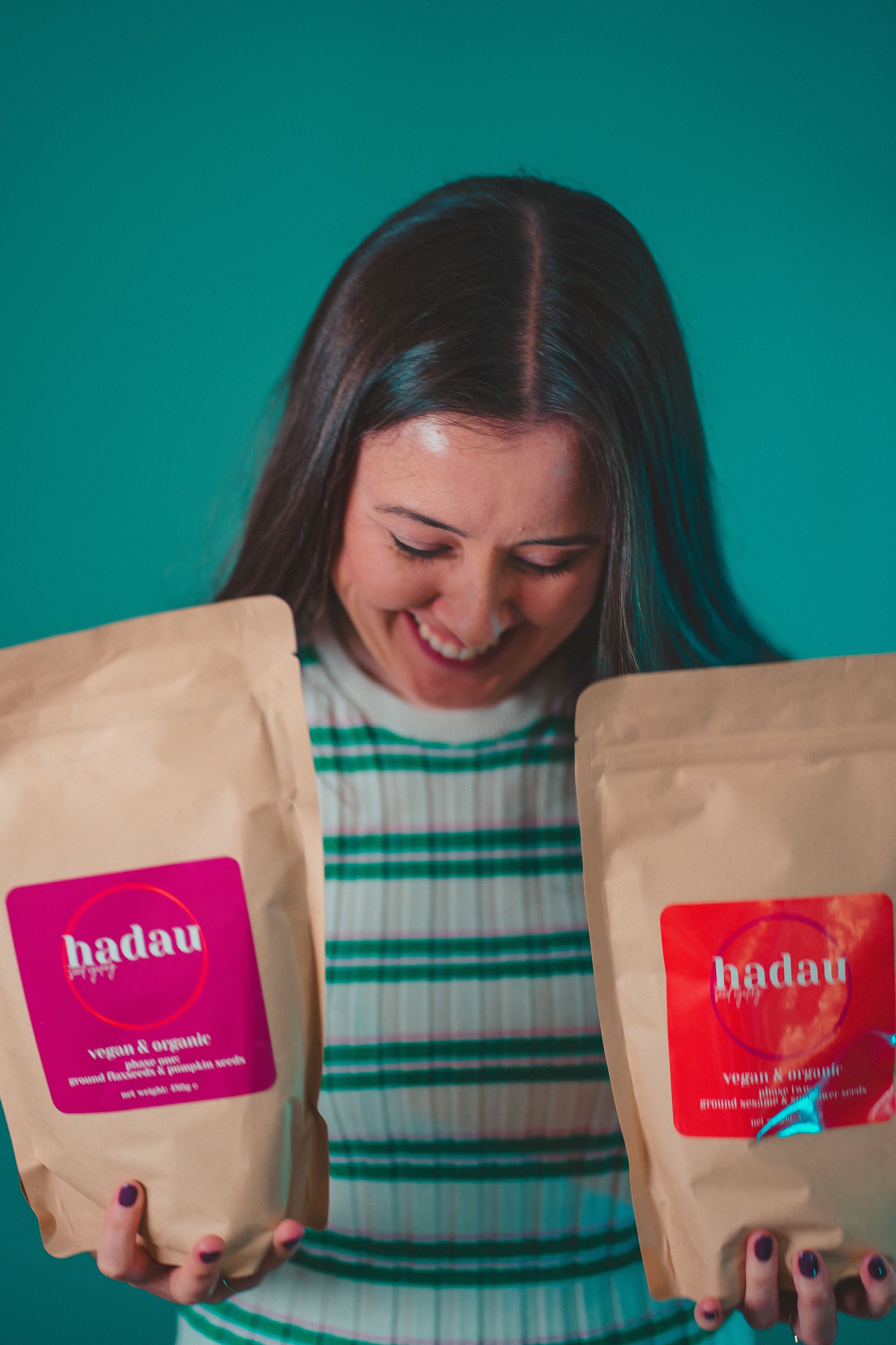 A woman smiling and looking down while holding two brown paper bags labeled 'hadau,' which appear to contain vegan and organic products.