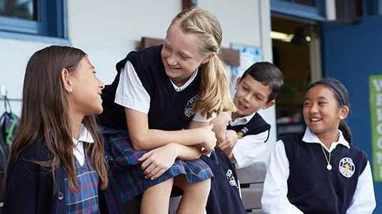 Four students in school uniforms laughing and chatting outside a school building.