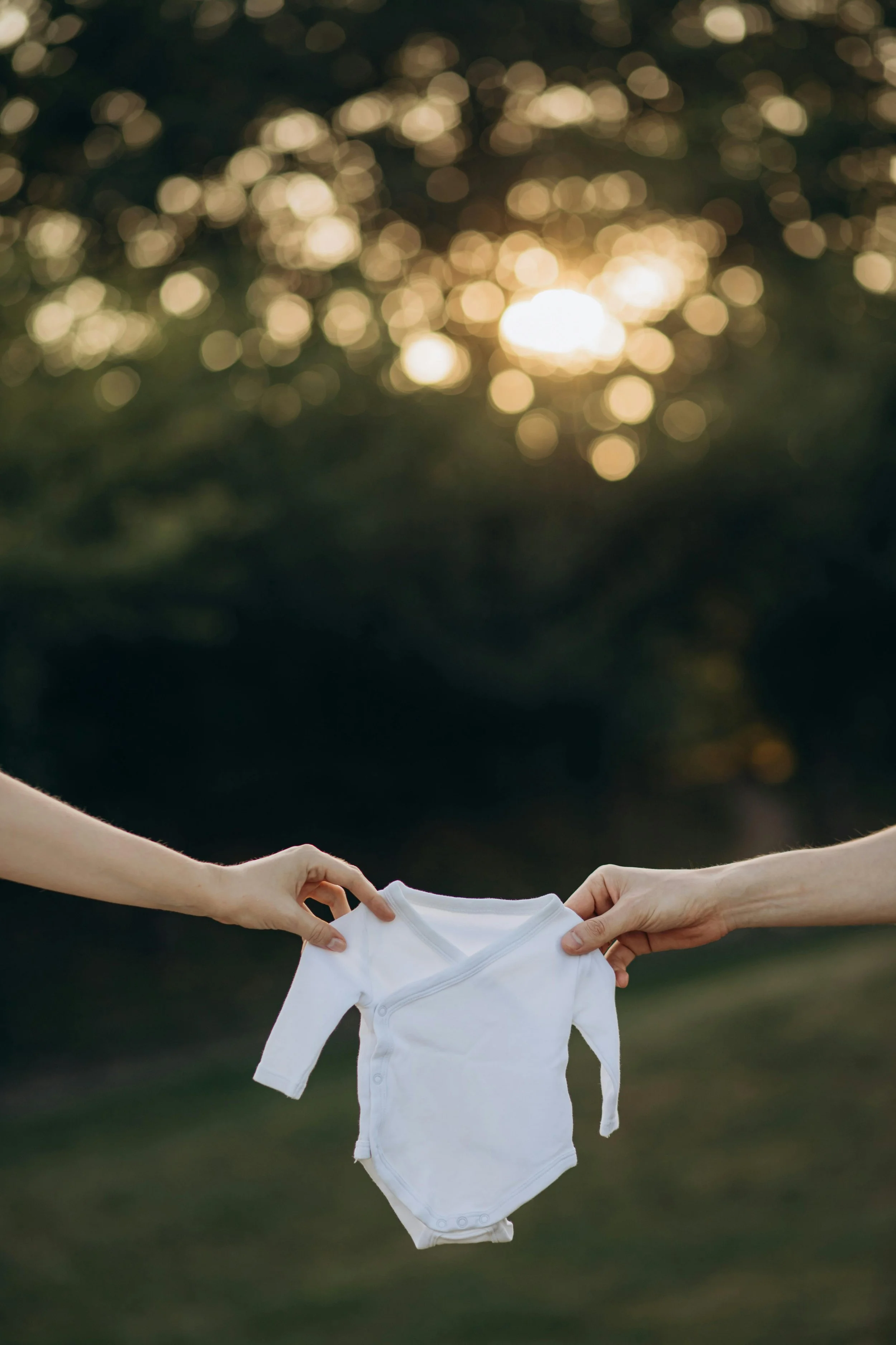 Two parents-to-be holding a white baby grown outside in garden in Exmouth, East Devon