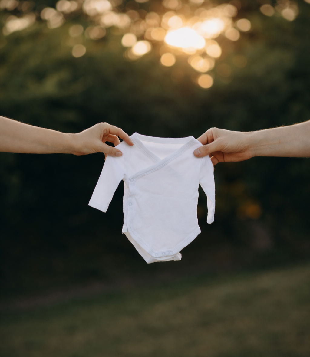 Two hands holding a white baby onesie outdoors at sunset in exmouth, devon
