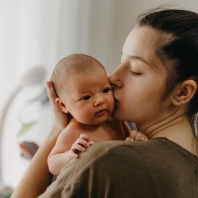 Mother kissing her newborn baby on head. she is standing up with her newborn baby over her shoulder