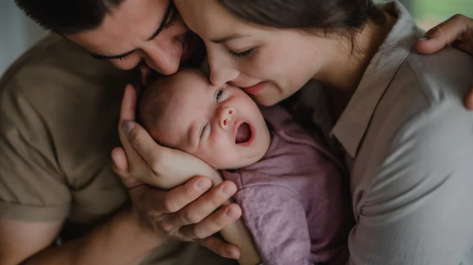 A family with a newborn baby, father and mother embracing and kissing the baby.