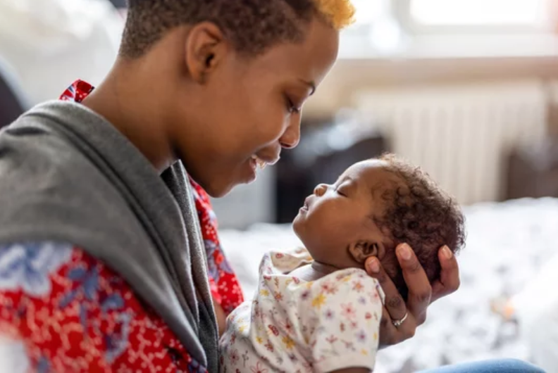 A young woman gently holding a baby girl and smiling at her.