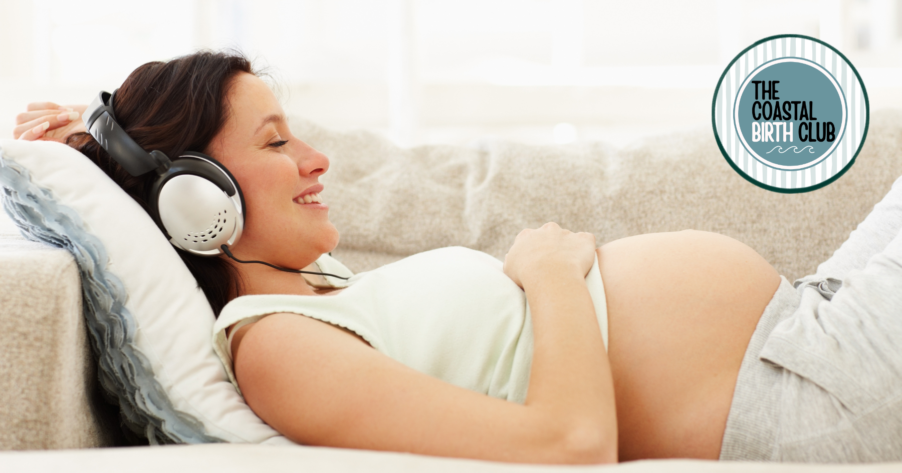 Pregnant woman lying on a couch, smiling, wearing headphones, with her hand on her baby bump, in a cozy home setting, with a logo for The Coastal Birth Club in the top right corner.