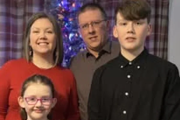 A family of four standing in front of a decorated Christmas tree, smiling at the camera.