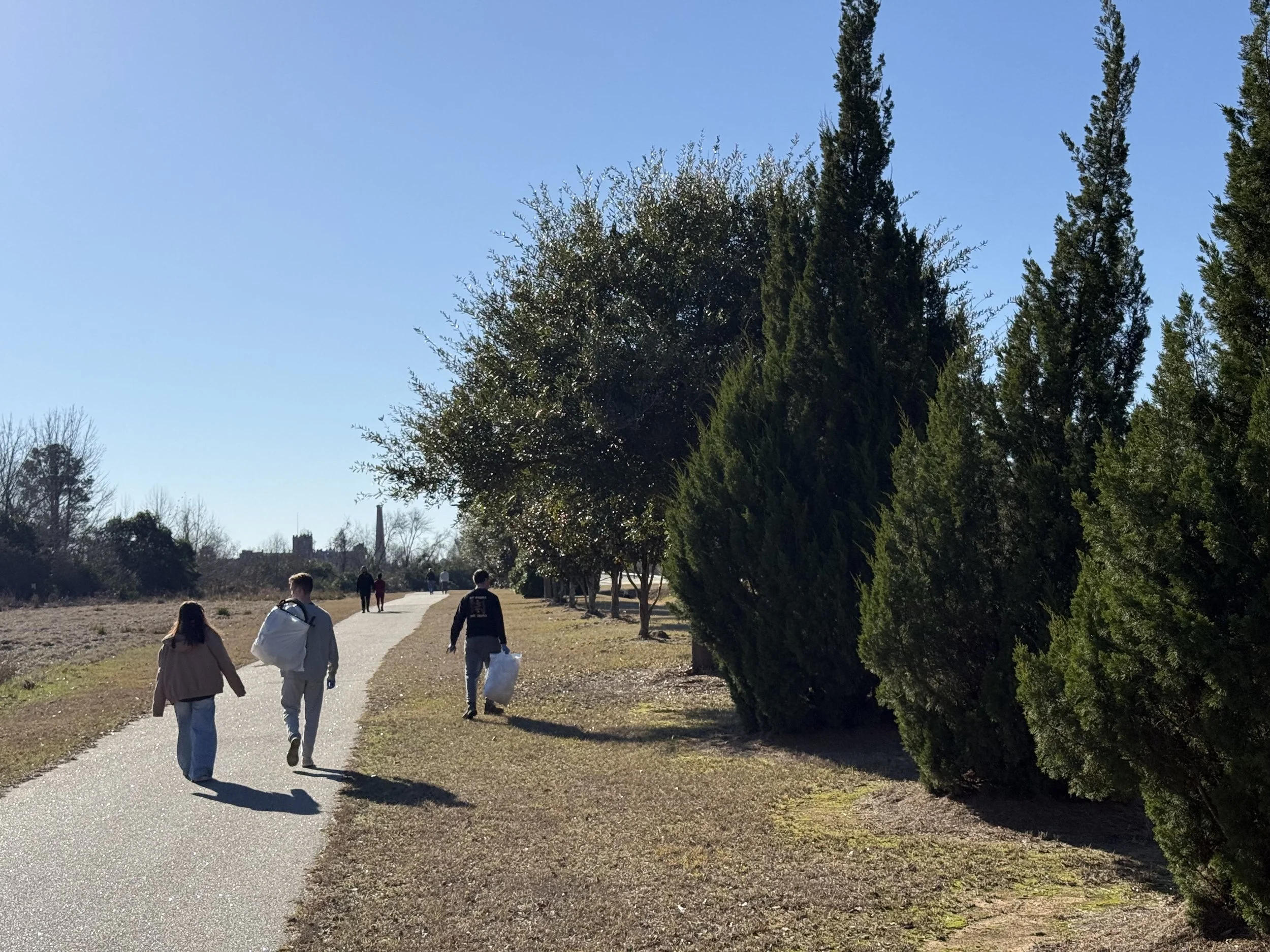 People walking on a paved pathway in a park with trees on the side and a clear blue sky.
