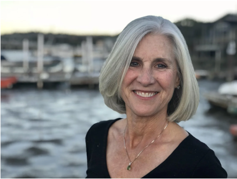 Smiling older woman with gray hair at a marina with boats on the water in the background