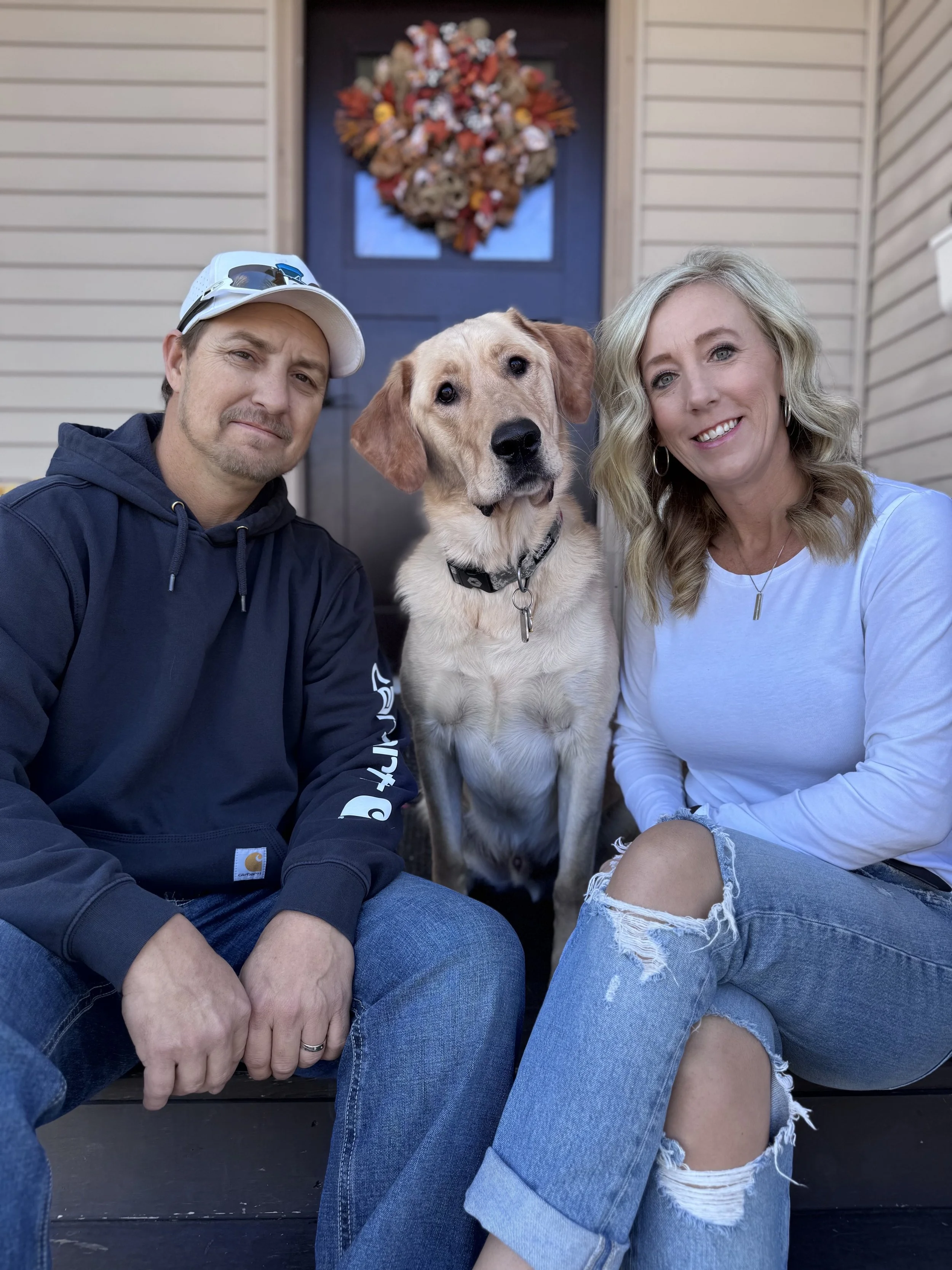 A man, woman, and a yellow Labrador Retriever sitting on staircase in front of a house with a decorated door.