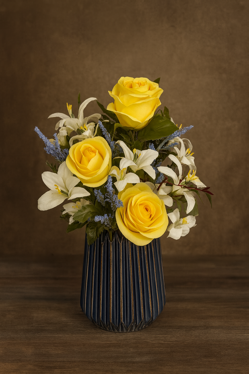 A floral arrangement with three yellow roses, white lilies, and small purple flowers in a dark striped vase on a wooden surface.