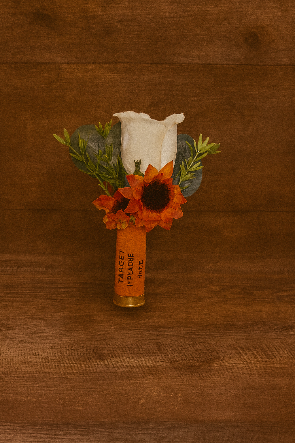 A floral arrangement with a white rose, orange flowers, and green foliage in a shotgun shell.