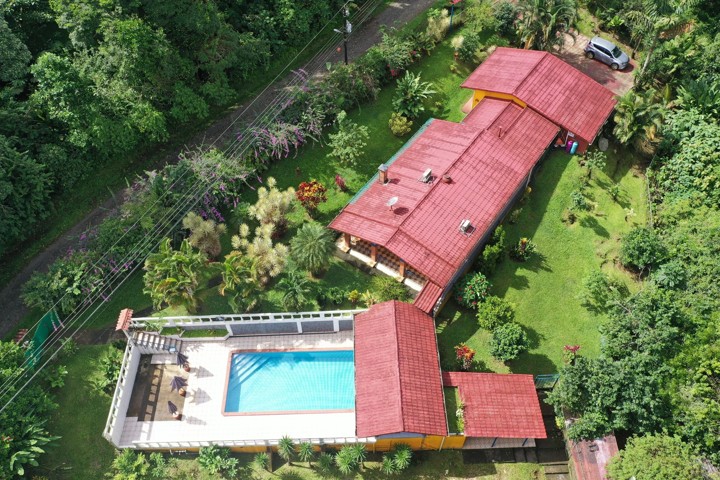 Aerial view of a house with a red roof, surrounded by Costa Rica jungle. There is a swimming pool and a guest house. The property is for sale. Income property with home and airbnb