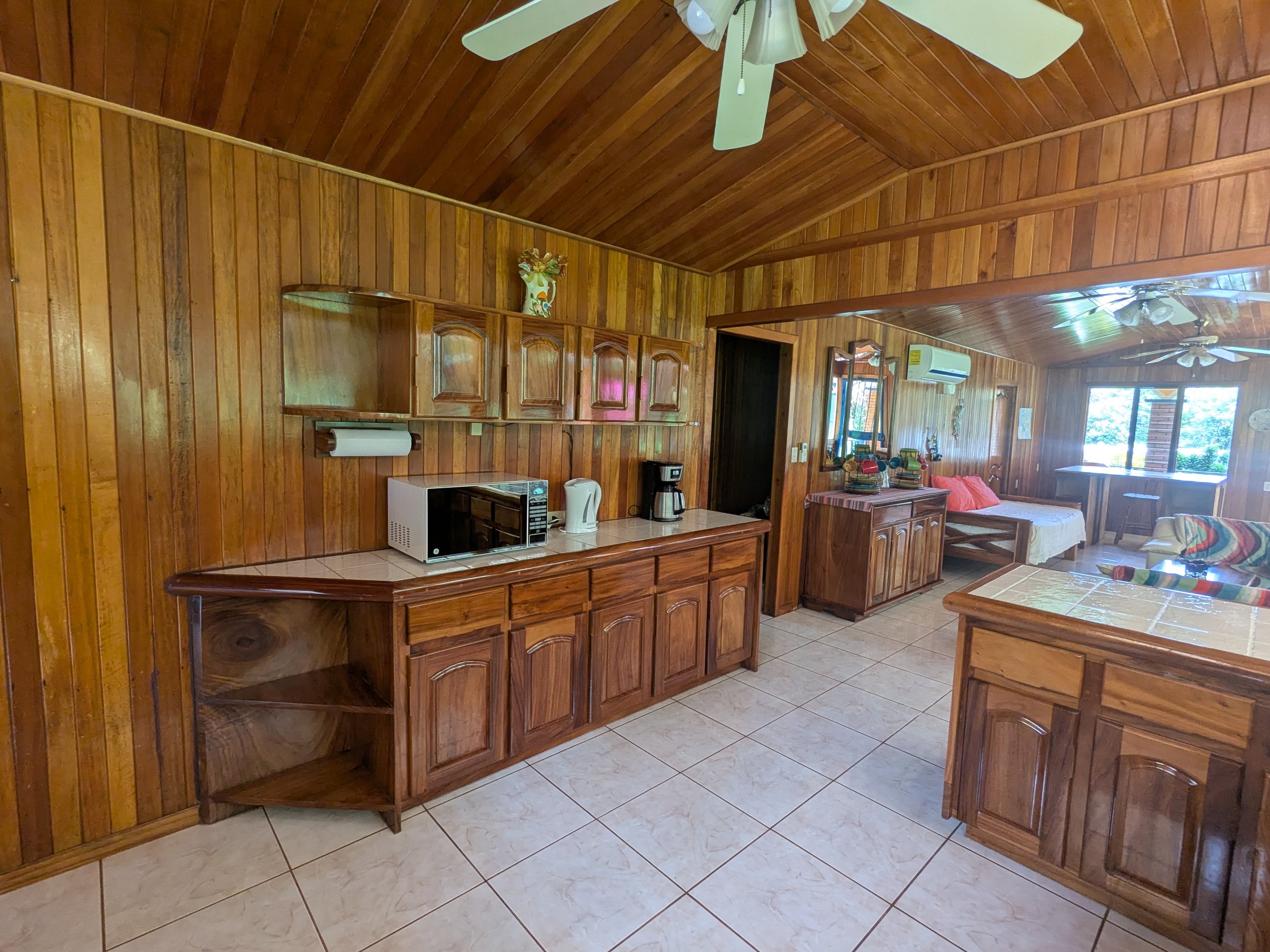 Wood-paneled kitchen and living area with tile flooring, ceiling fans, and large windows with outdoor views.