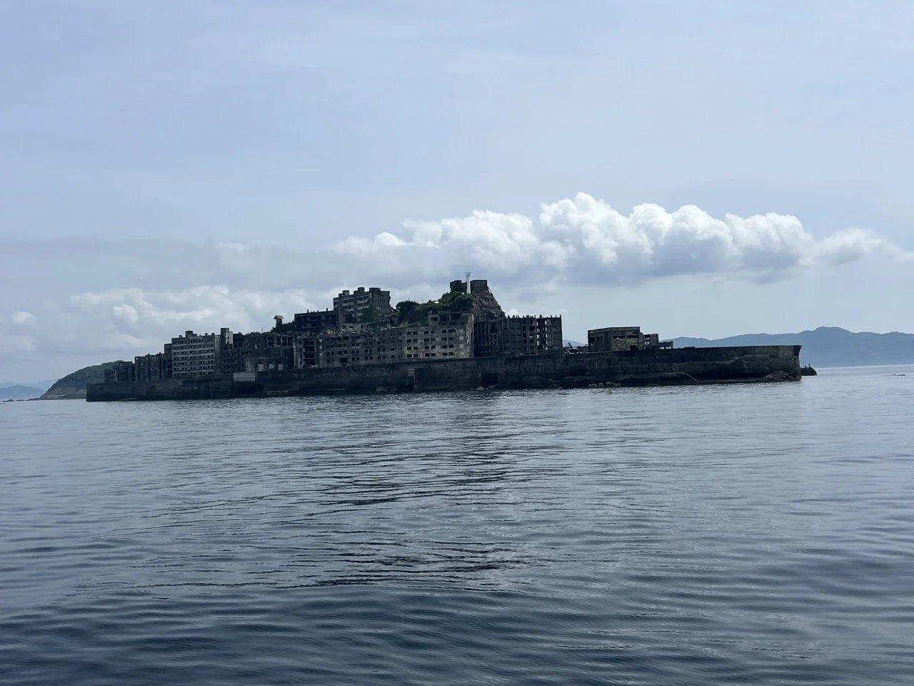 A massive island covered in tall concrete ruins, long abandoned, as seen from a boat traveling around it.