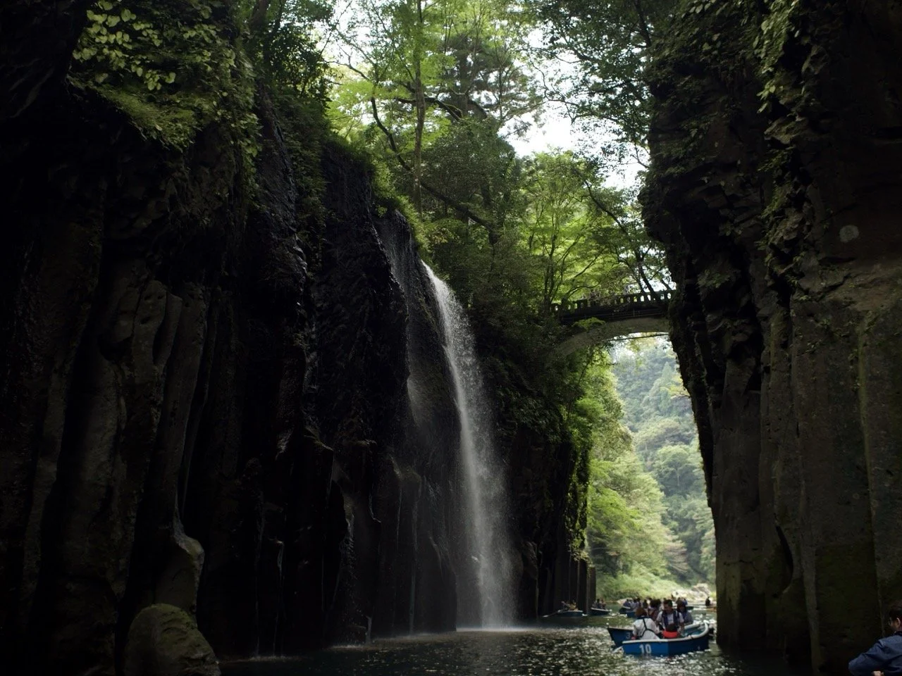 View from a boat sailing through a gorge looking up at a waterfall and a bridge crossing it.