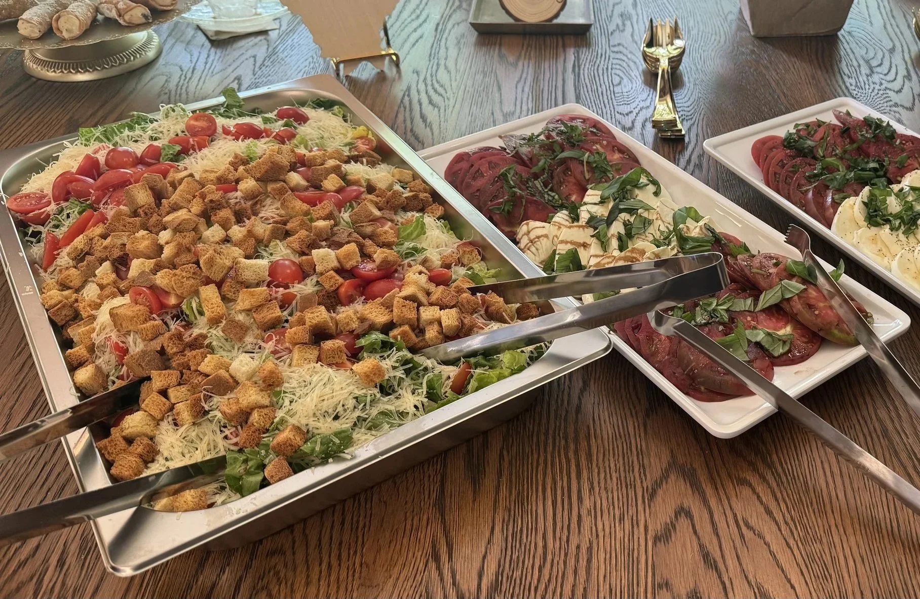 Salad with cherry tomatoes, shredded cheese, croutons, and lettuce next to plates of sliced tomatoes and mozzarella with basil.