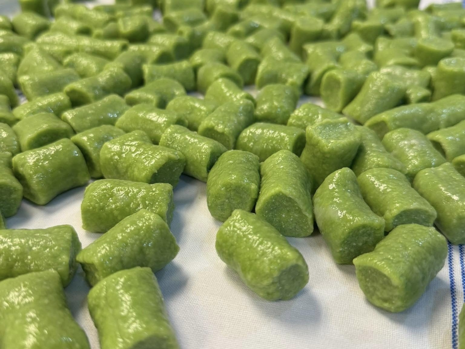 Close-up of green gnocchi coated in sauce, spread on a white cloth