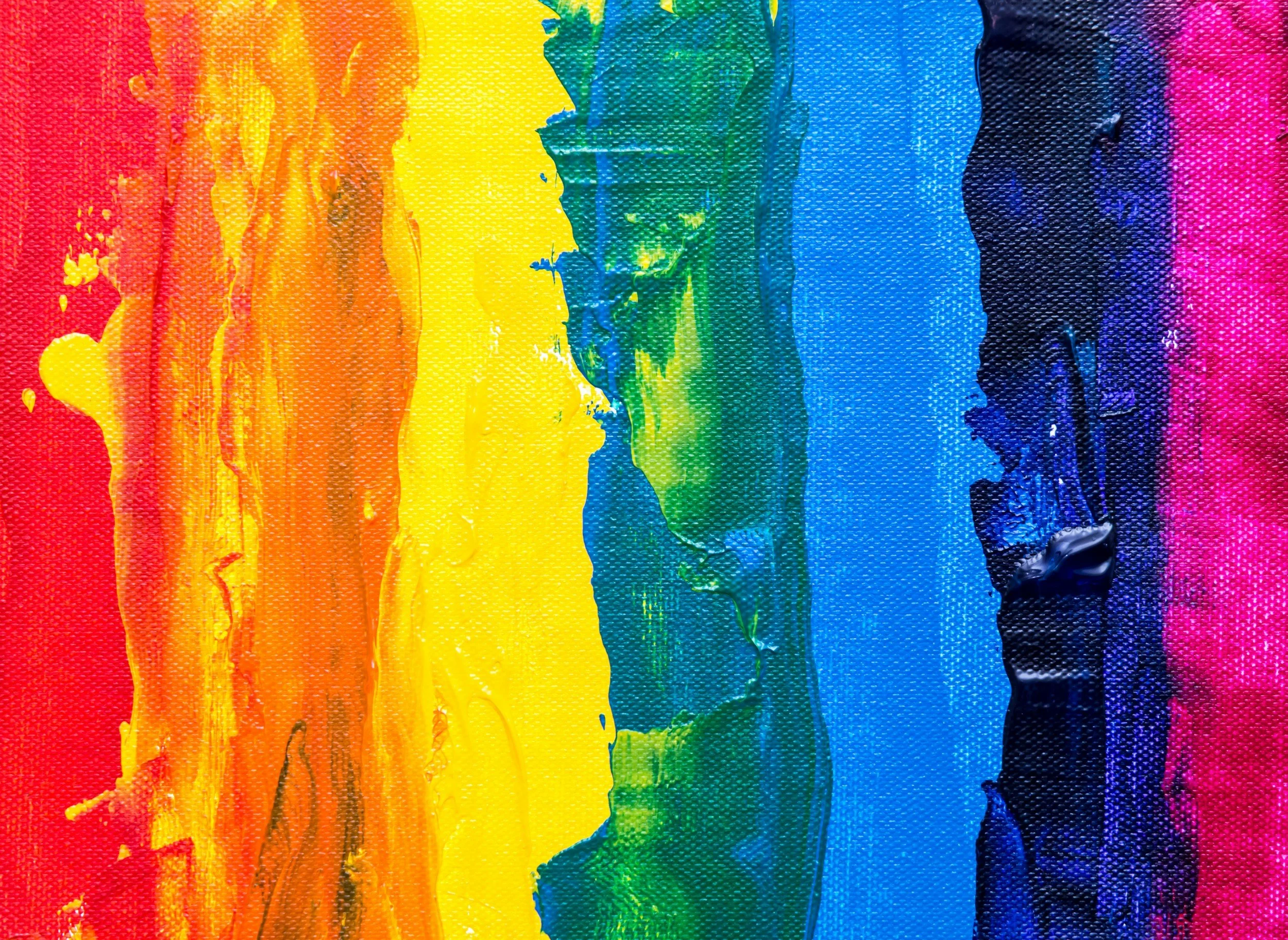 Close-up of an abstract painting featuring broad, textured brushstrokes in rainbow colors, including red, orange, yellow, green, blue, and purple.