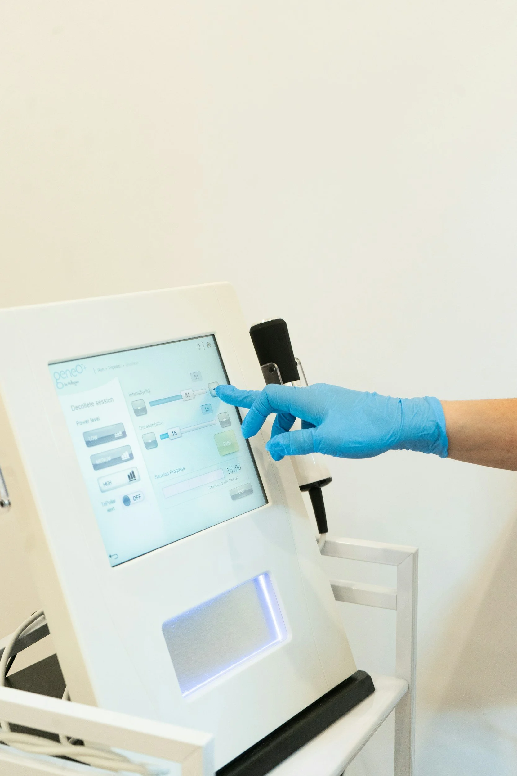 A person wearing a blue glove presses a button on a medical device touchscreen monitor in a clinical setting.
