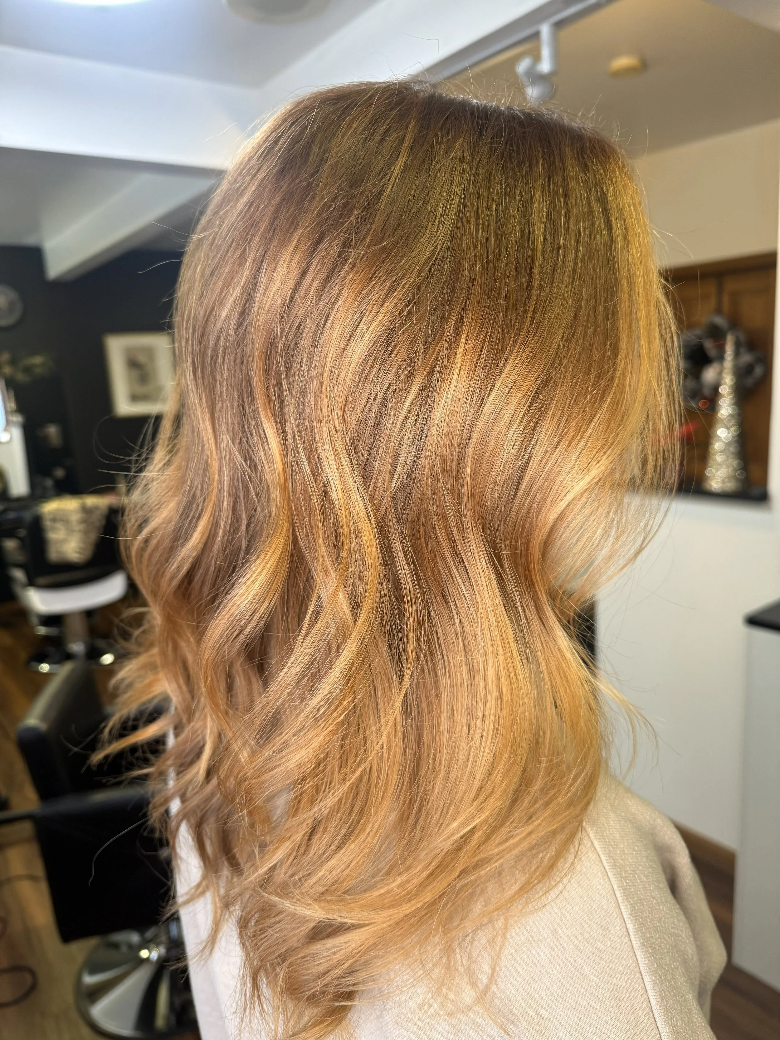 Side view of a woman with shoulder-length, wavy, strawberry blonde hair in a salon.