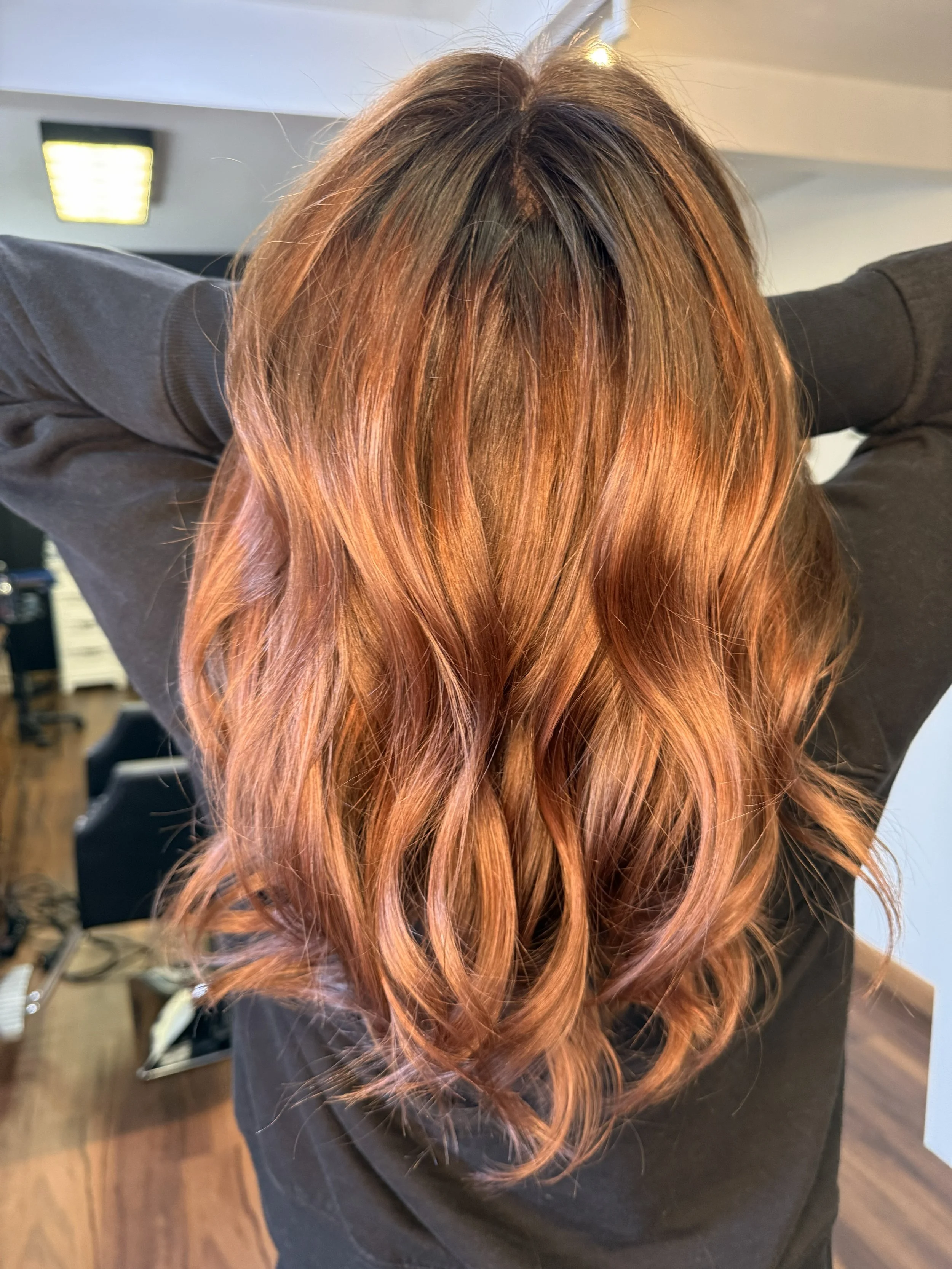 A person with long, wavy, copper-colored hair standing in a hair salon.