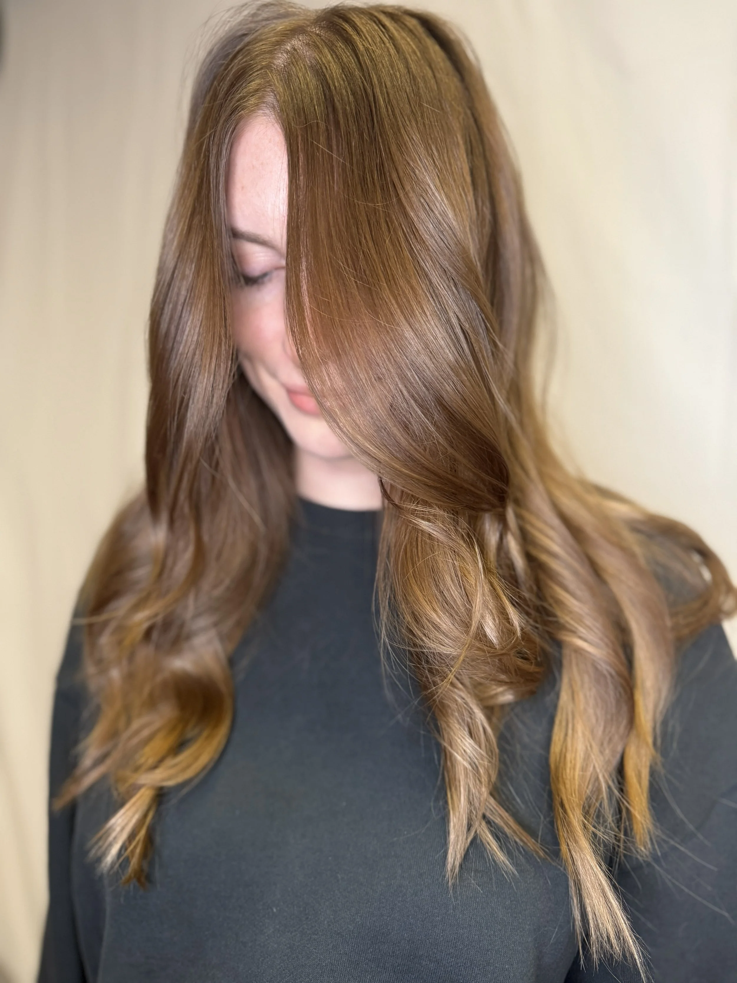 A woman with long, wavy red hair looking down, wearing a black top.