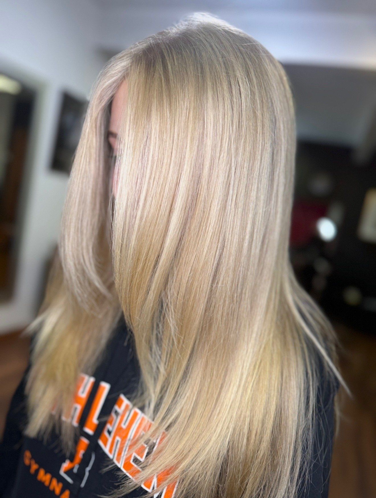 Close-up of a woman with straight, blonde hair with subtle highlights, showcasing her styled hair from the side.