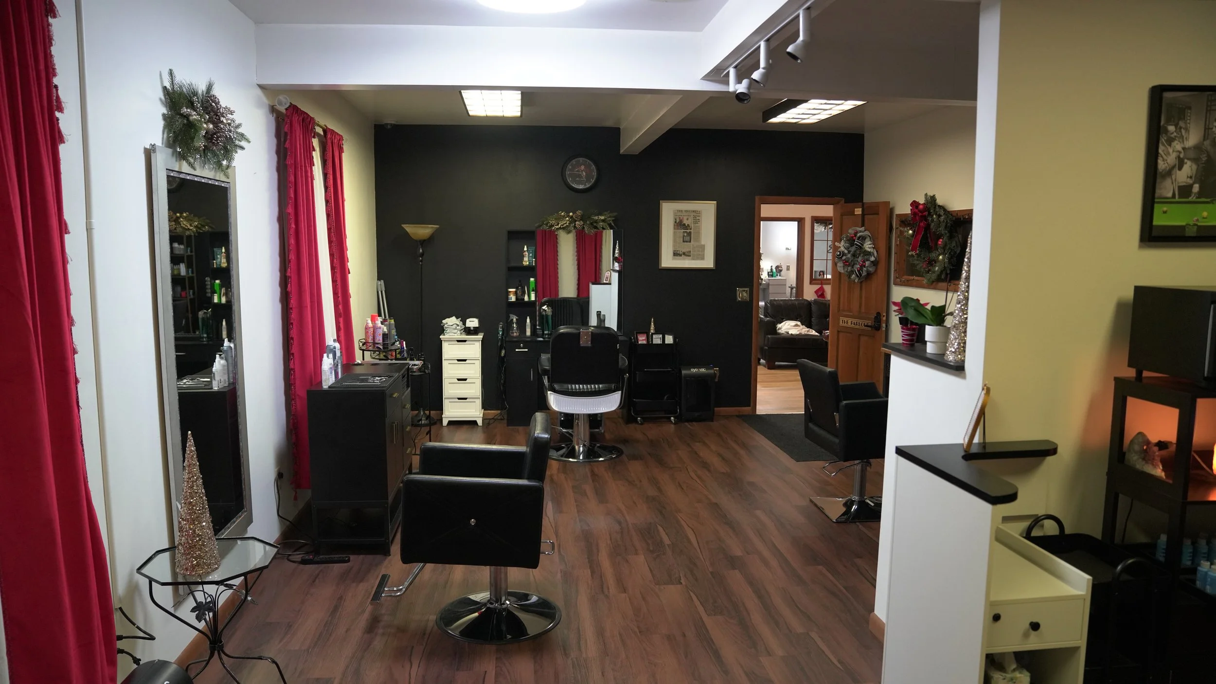 A hair salon decorated for Christmas with red curtains, wreaths, and holiday decorations. Includes styling chairs, mirrors, and hair products.