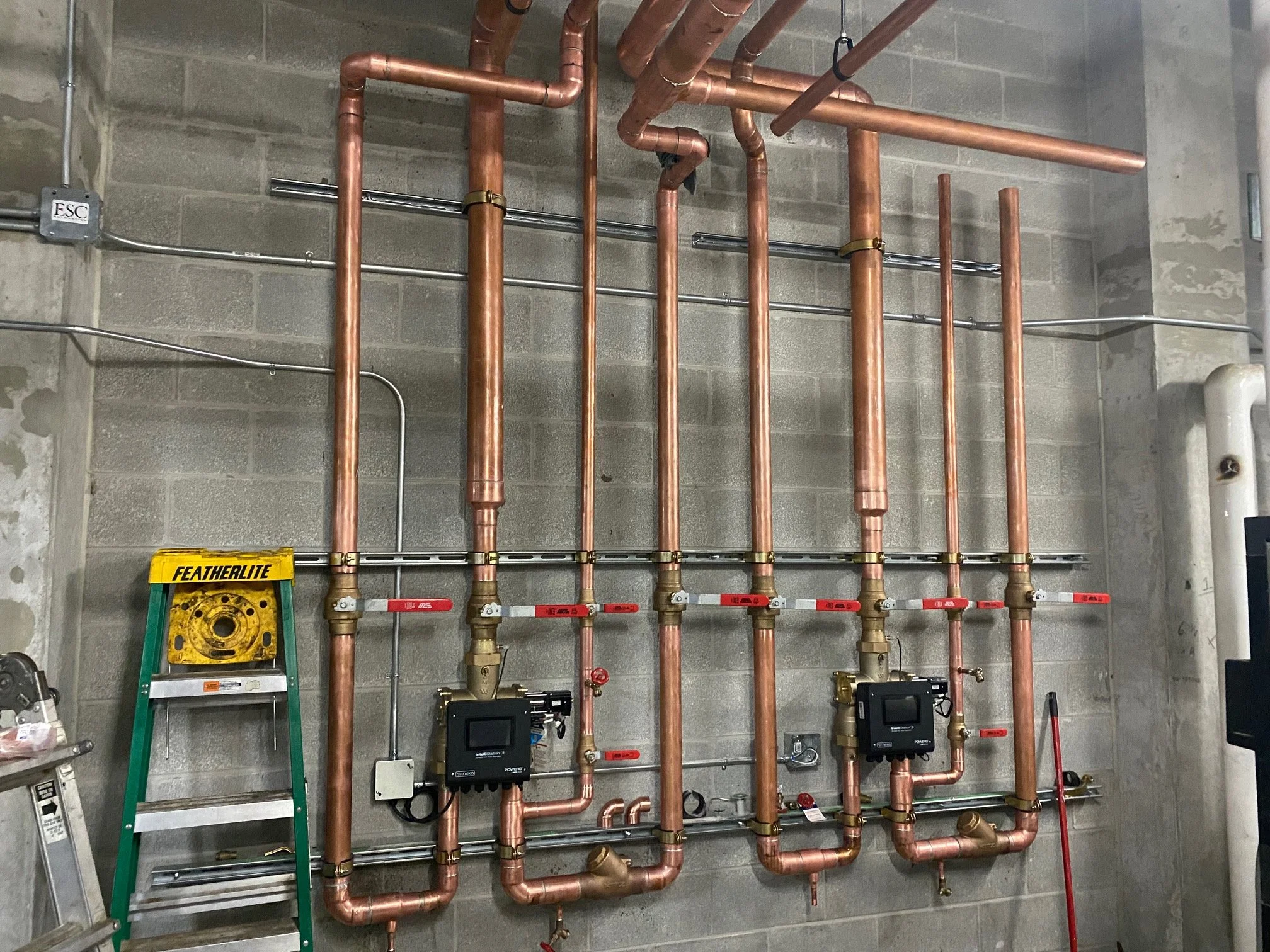 Industrial plumbing system with copper pipes, valves, and electronic controls mounted on a concrete wall.
