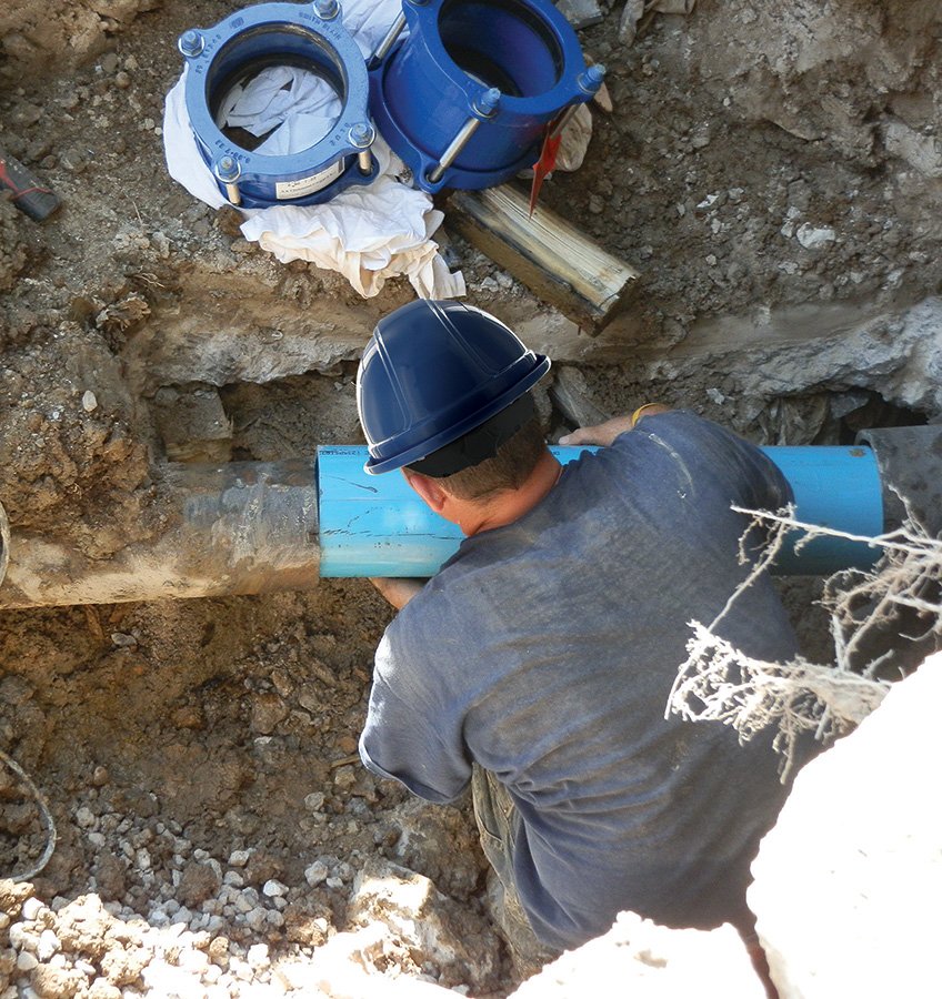 Worker in a hard hat installing or repairing a large blue pipe underground.