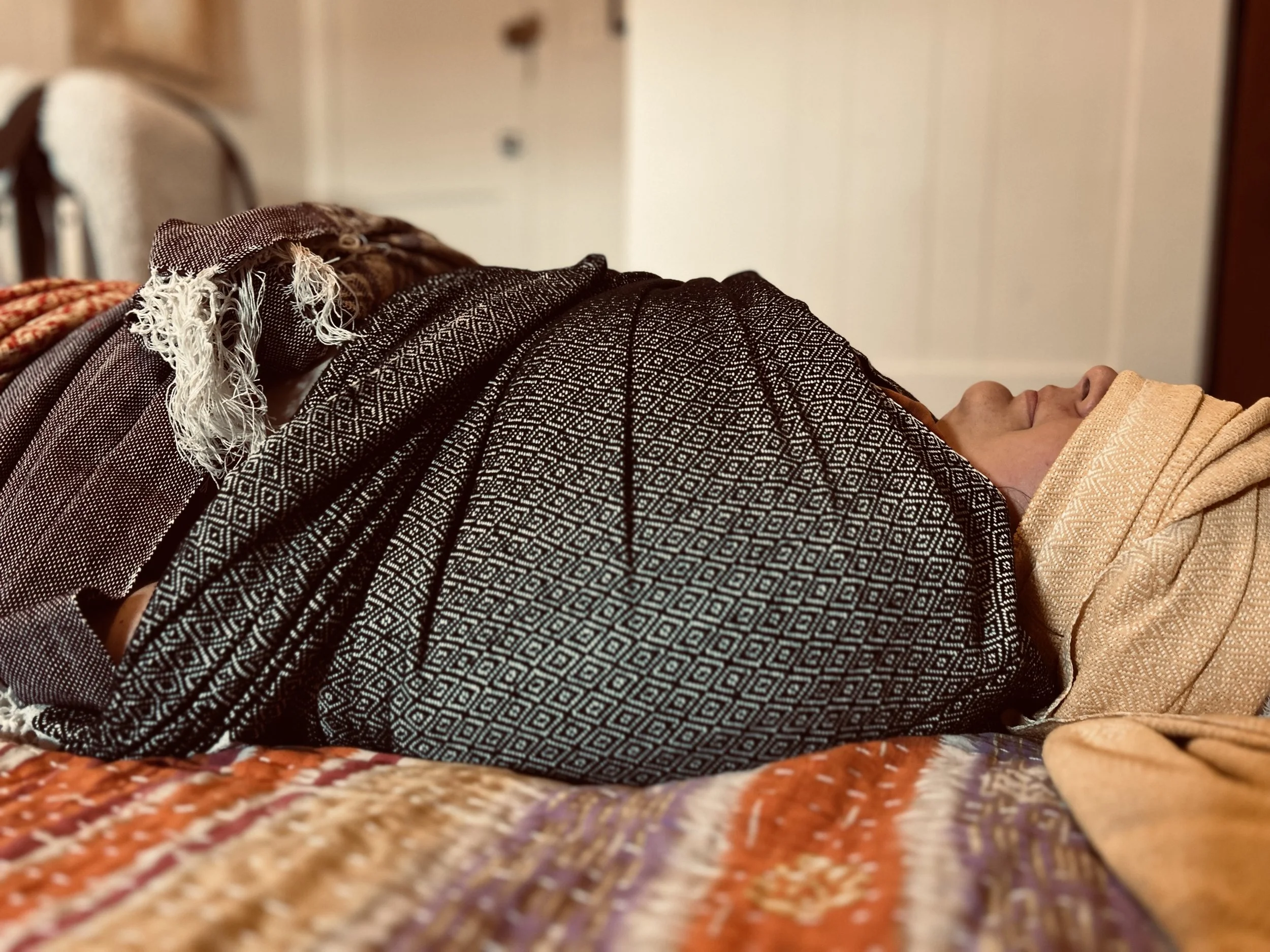 Woman resting while wrapped in rebozos during a closing bodywork session
