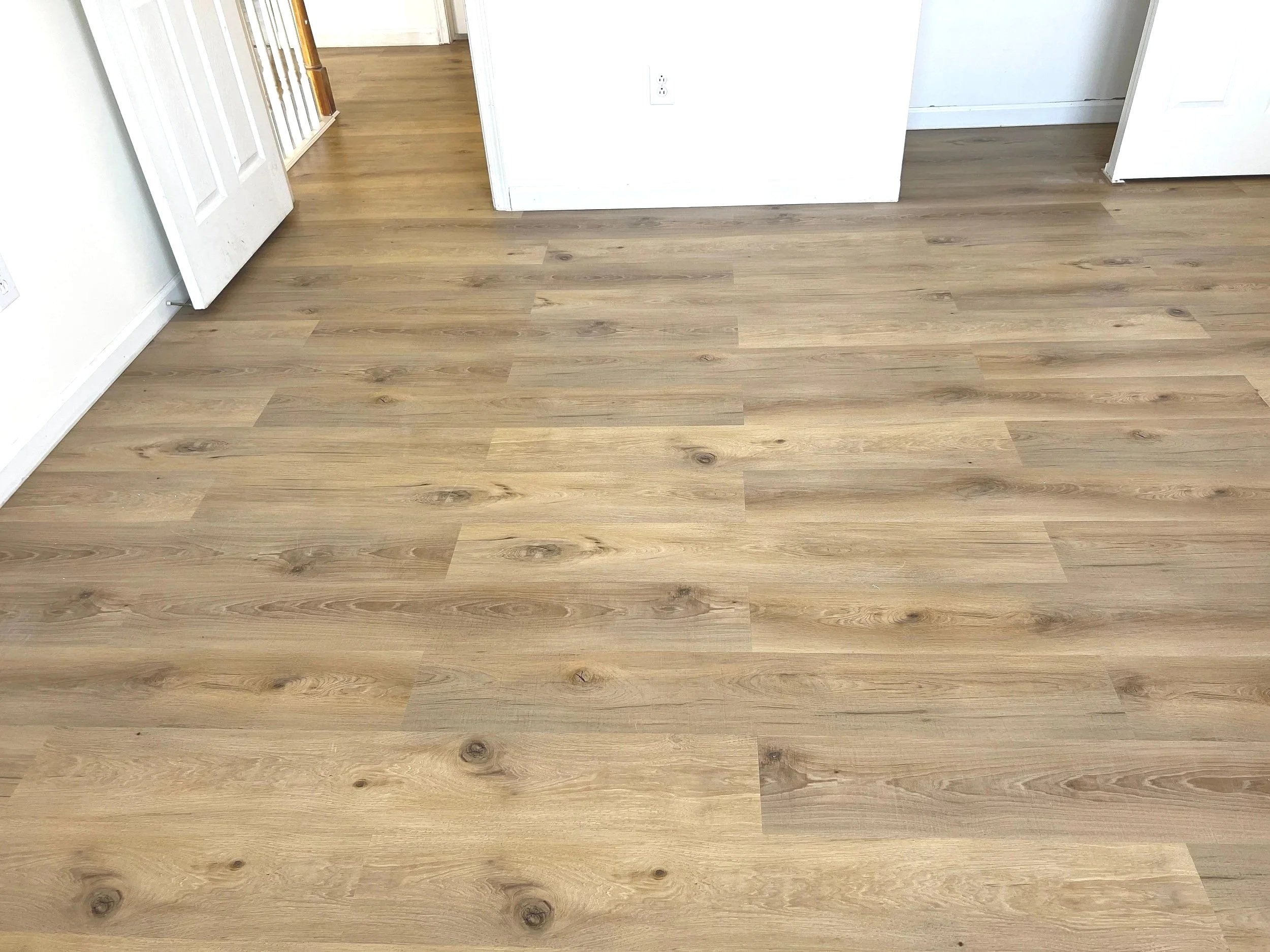Photo of a room with light wood flooring, white walls, and open white doors, showing an open-space interior.