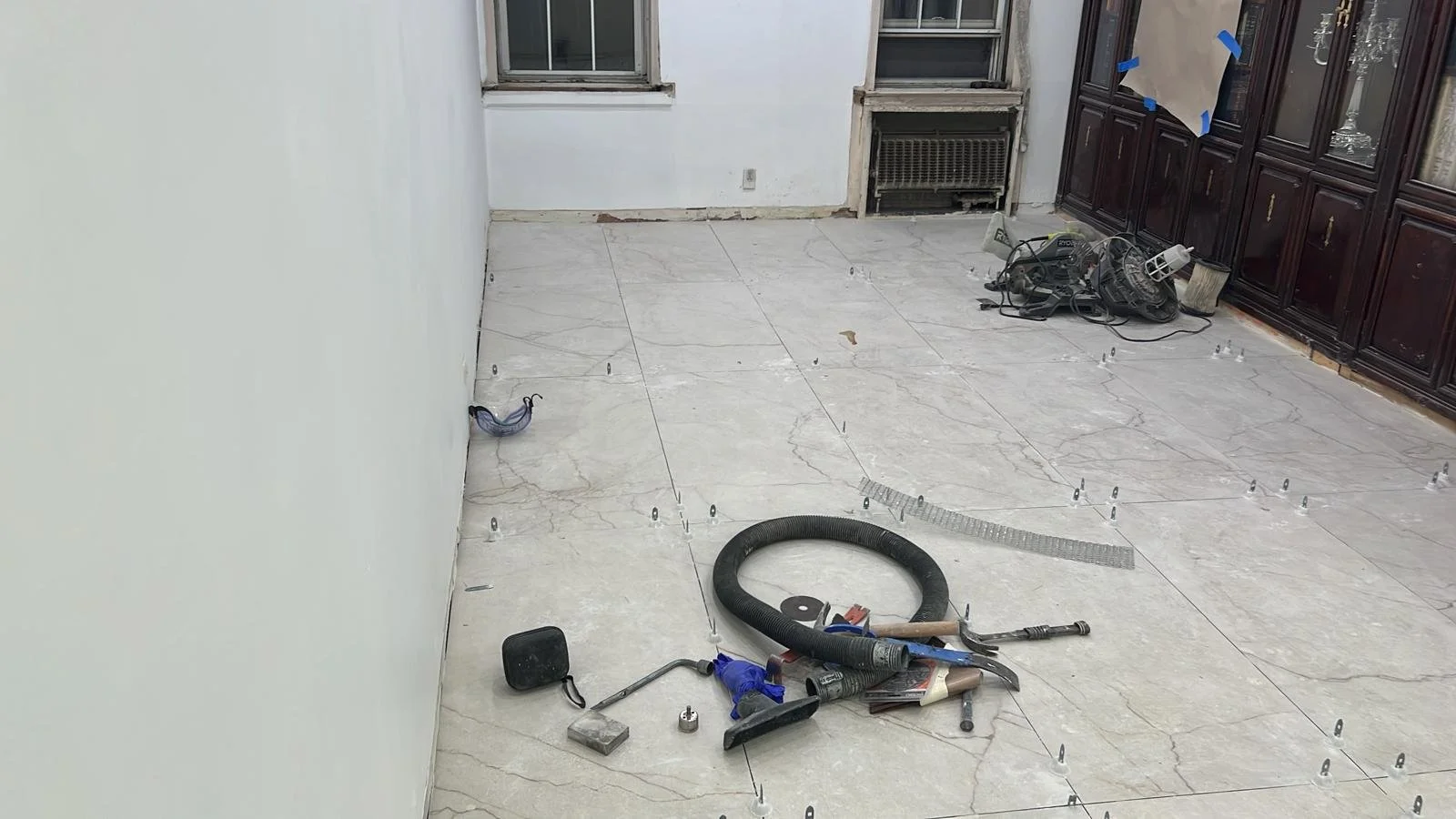 Room under renovation with tile flooring, construction tools, and equipment on the floor.