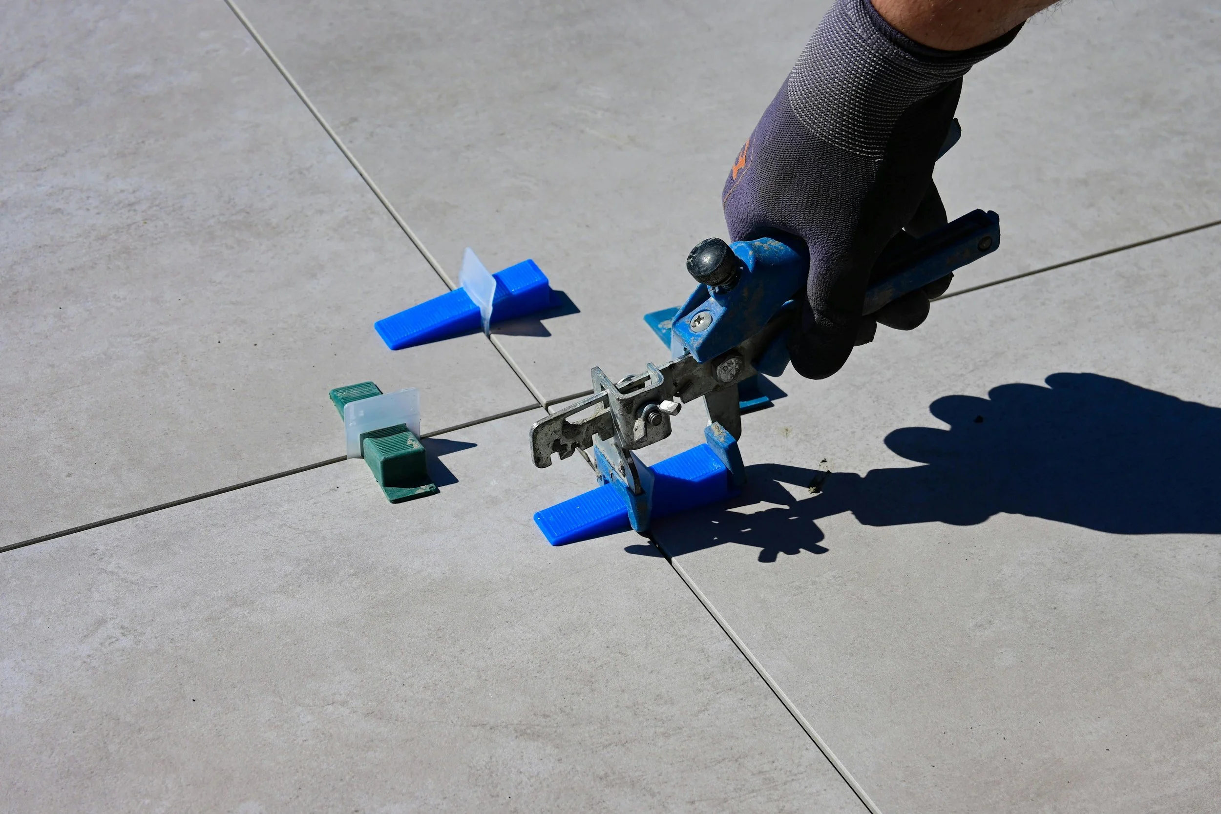 A person using a notched trowel to spread adhesive on a tiled floor.