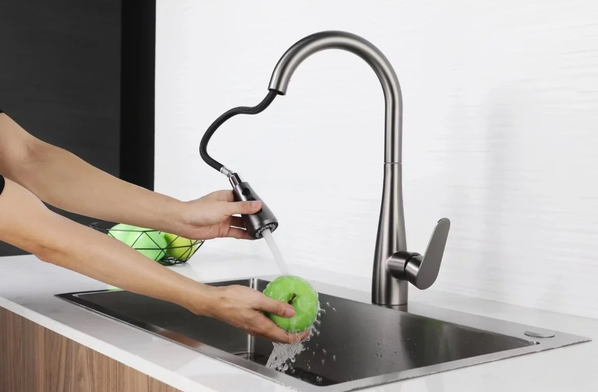 Person rinsing a green apple in a kitchen sink with a modern faucet, using a handheld sprayer.