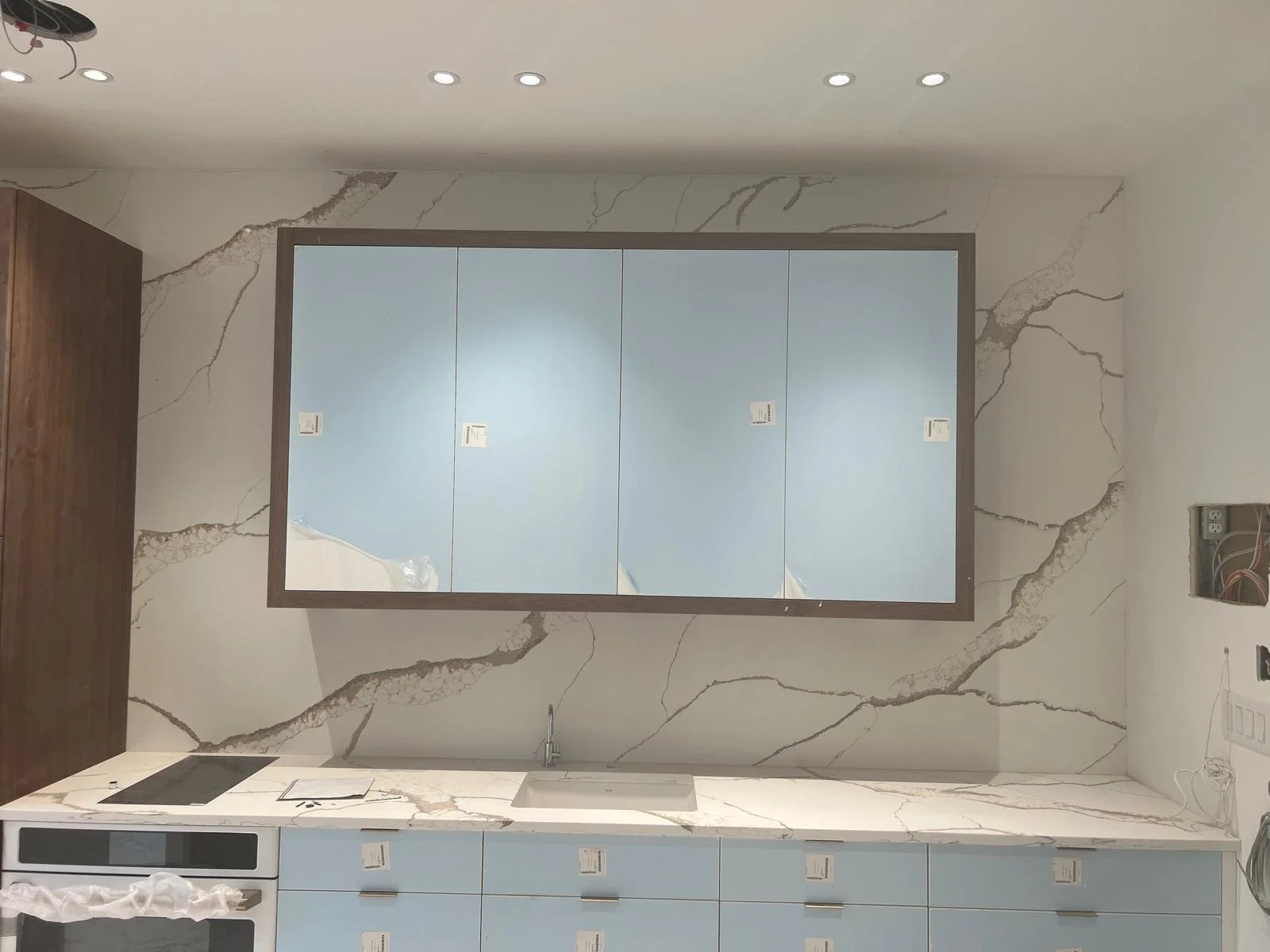 Kitchen with marble backsplash, on-trend blue cabinets, and a large mirror on the wall.