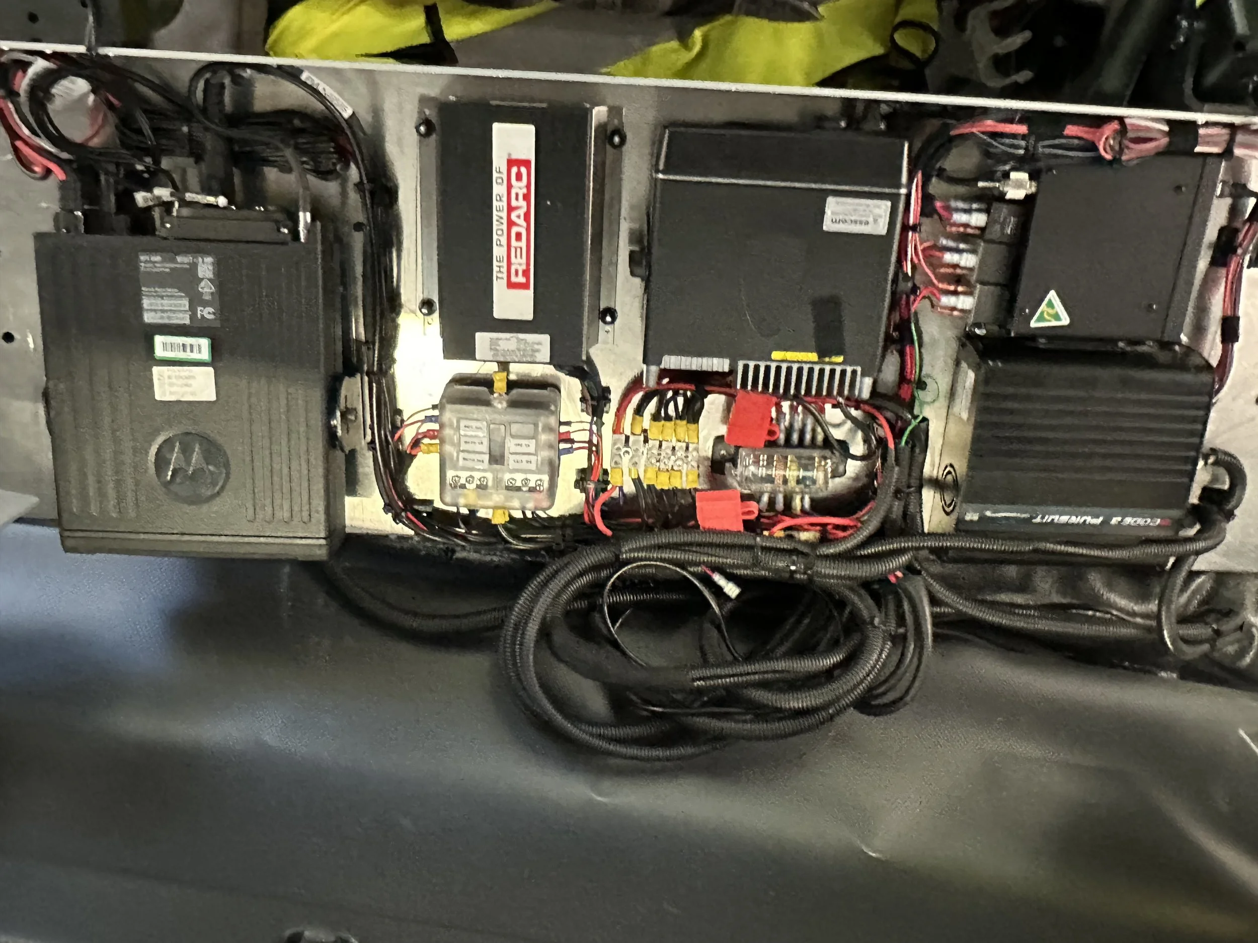 Custom-fit communications panel for NSW RFS vehicle with Motorola, Simoco SRM900, and GME UHF radios, Code 3 Pursuit controller, and Redarc 24–12V power converter installed behind the driver/passenger seat.