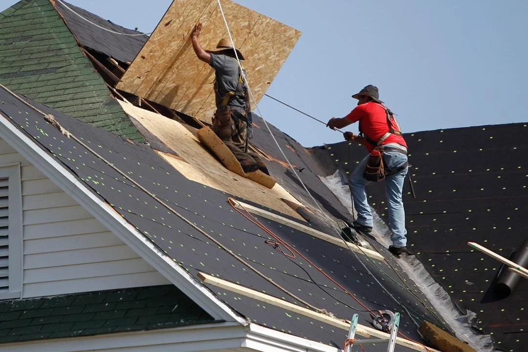 Roof replacement in progress on residential home with roofing contractors installing new shingles
