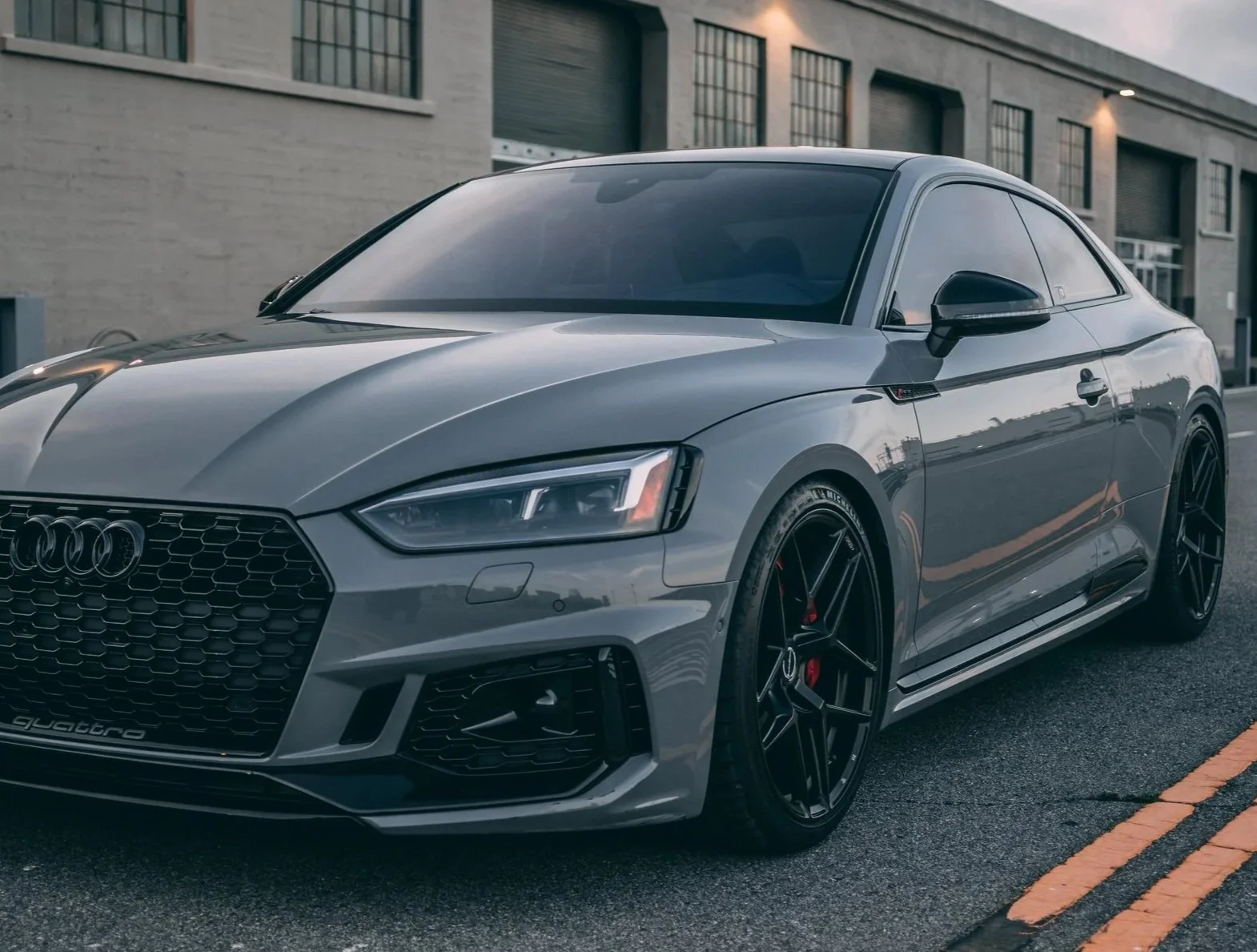 A silver Audi coupe car parked on a city street in front of a modern building.