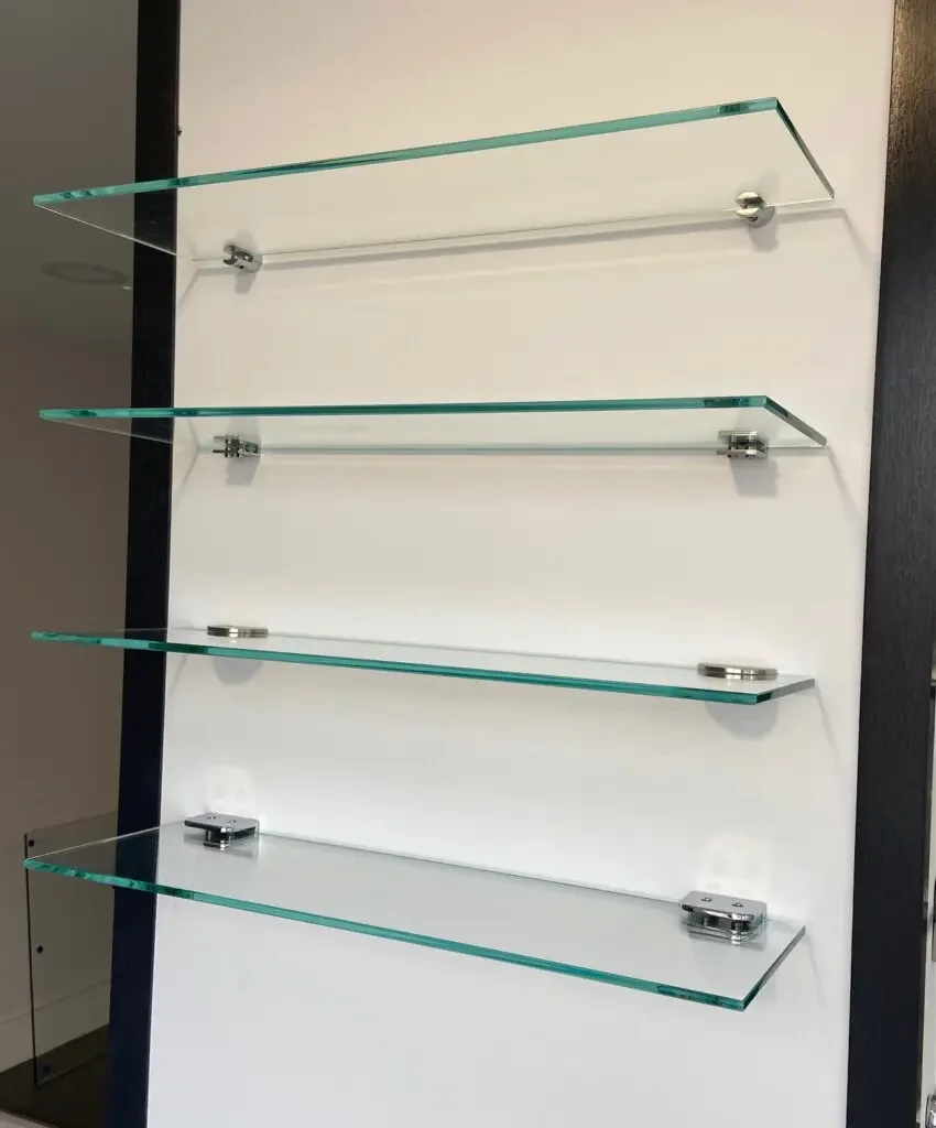Four glass shelves mounted on a white wall using metal brackets.